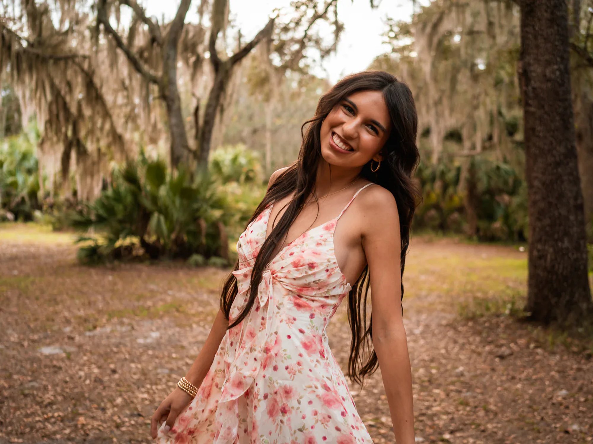 Close senior portrait of a smiling young woman in a pink floral dress.