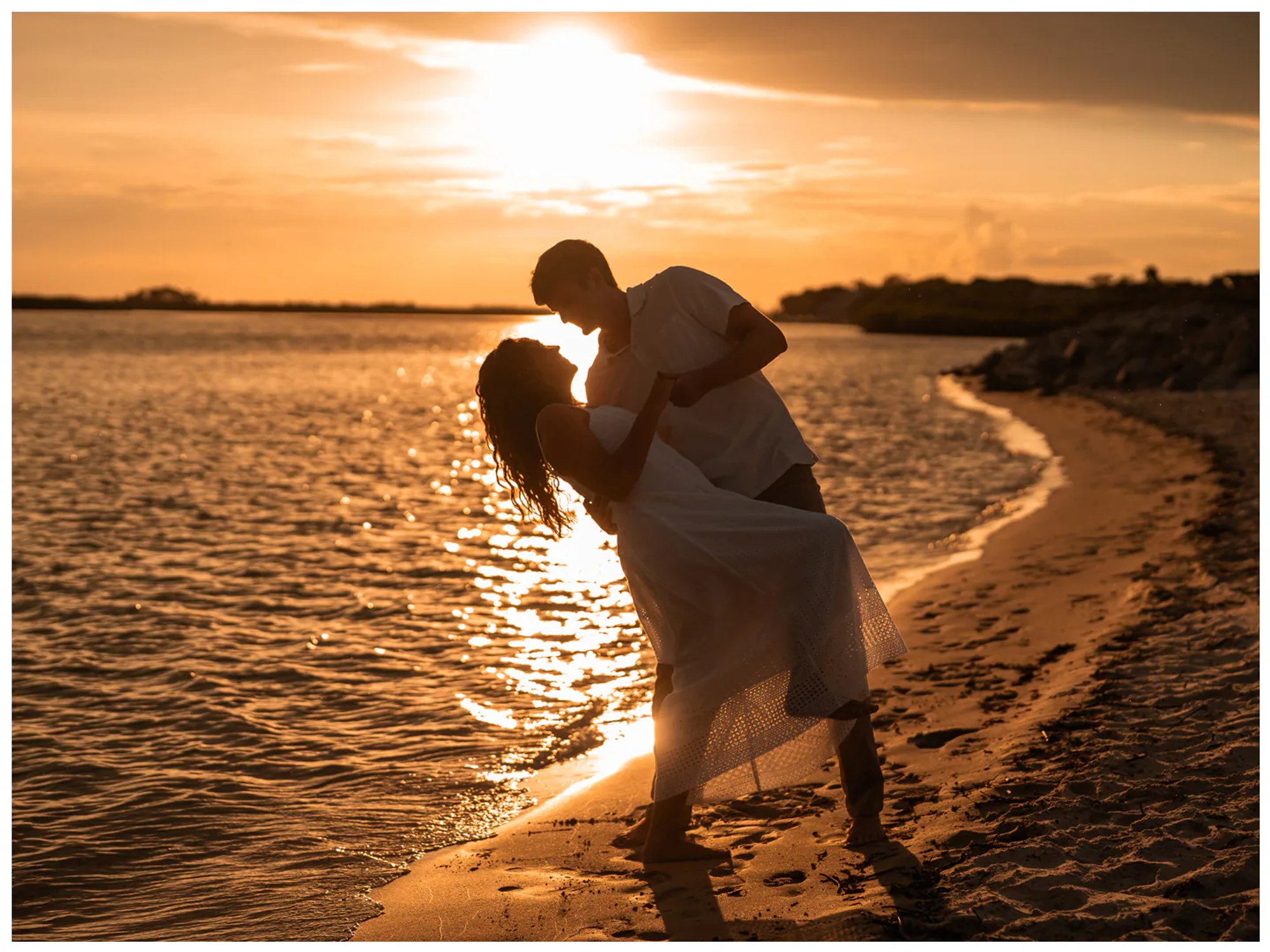 Man dipping his partner for a kiss along the golden shoreline.