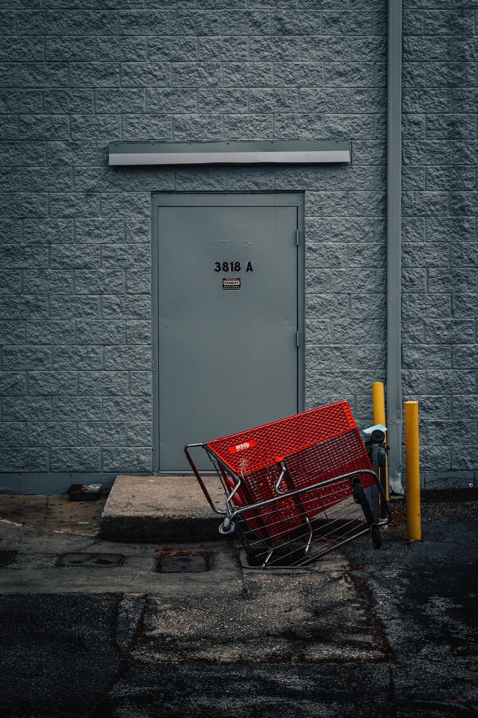 Red shopping cart tipped outside a gray service door.