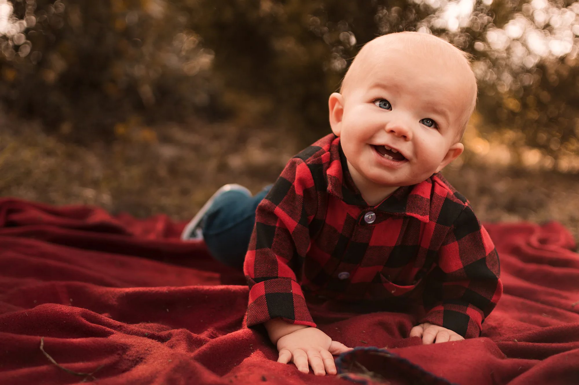 Smiling baby in red-and-black plaid lying on a red blanket.