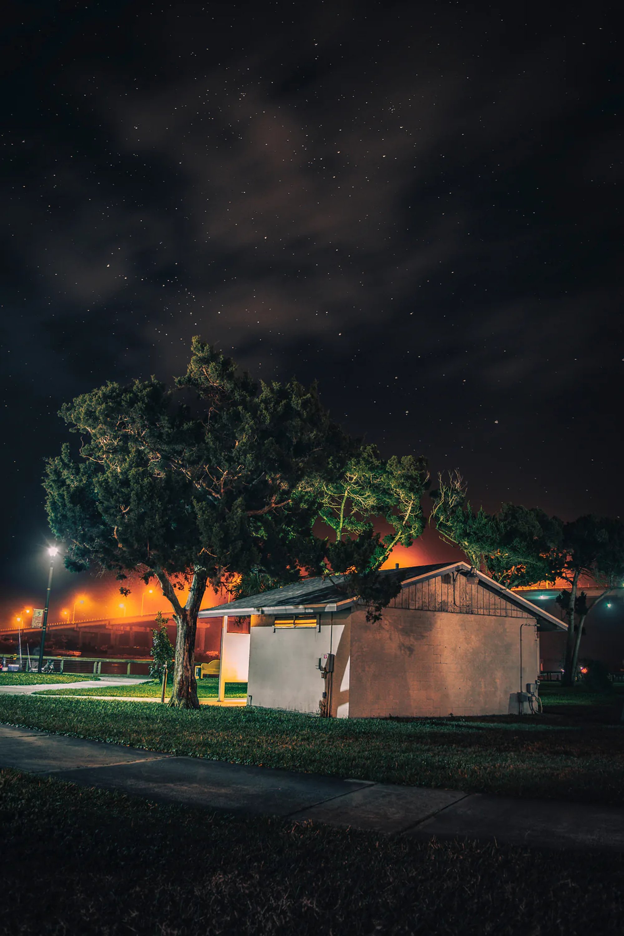 Small building and tree illuminated beneath dramatic nighttime clouds.