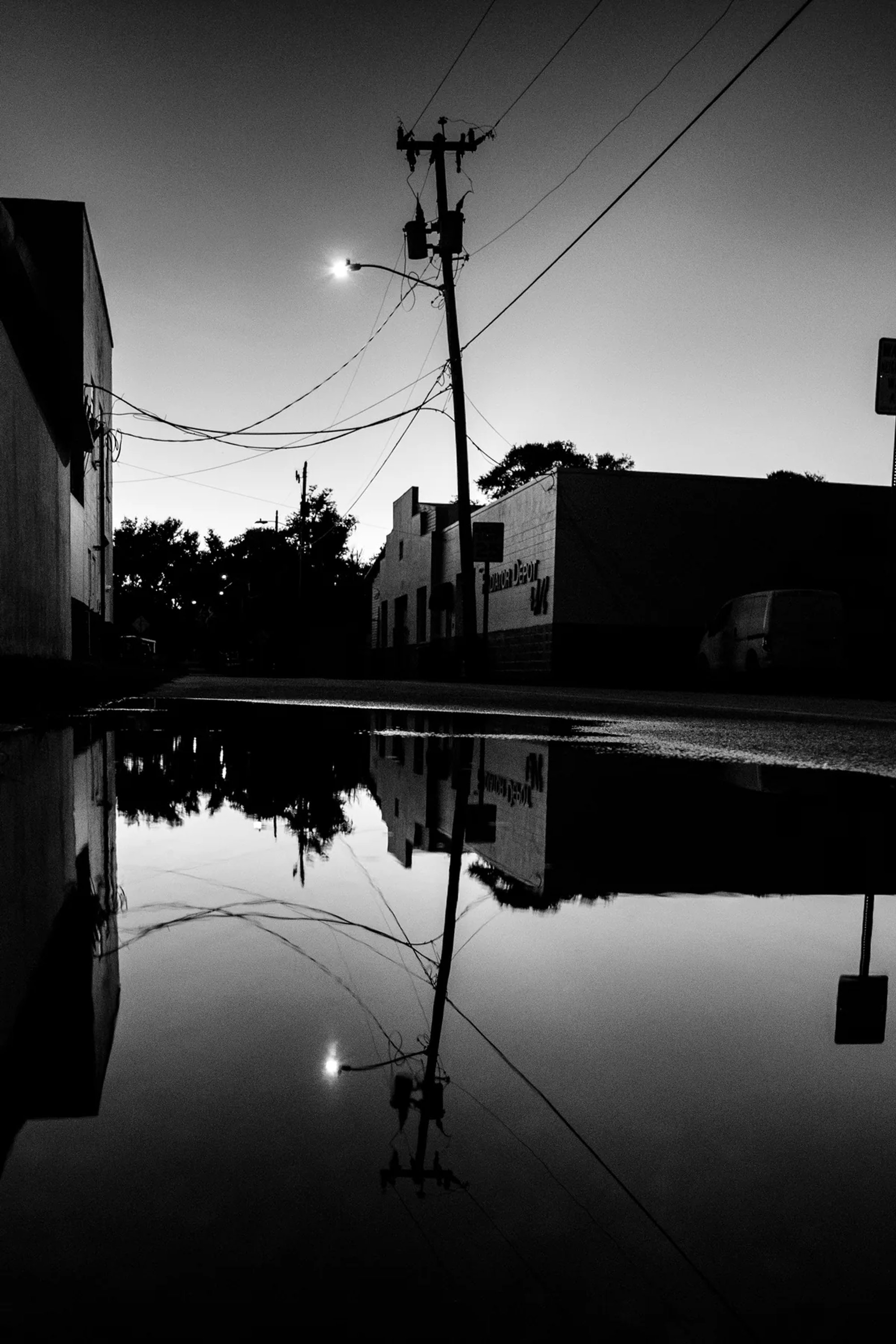 Utility pole and buildings reflected in still floodwater at dusk.