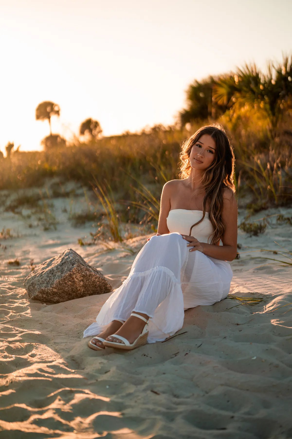 Young woman wearing a pink wrap over a white dress among coastal dunes.