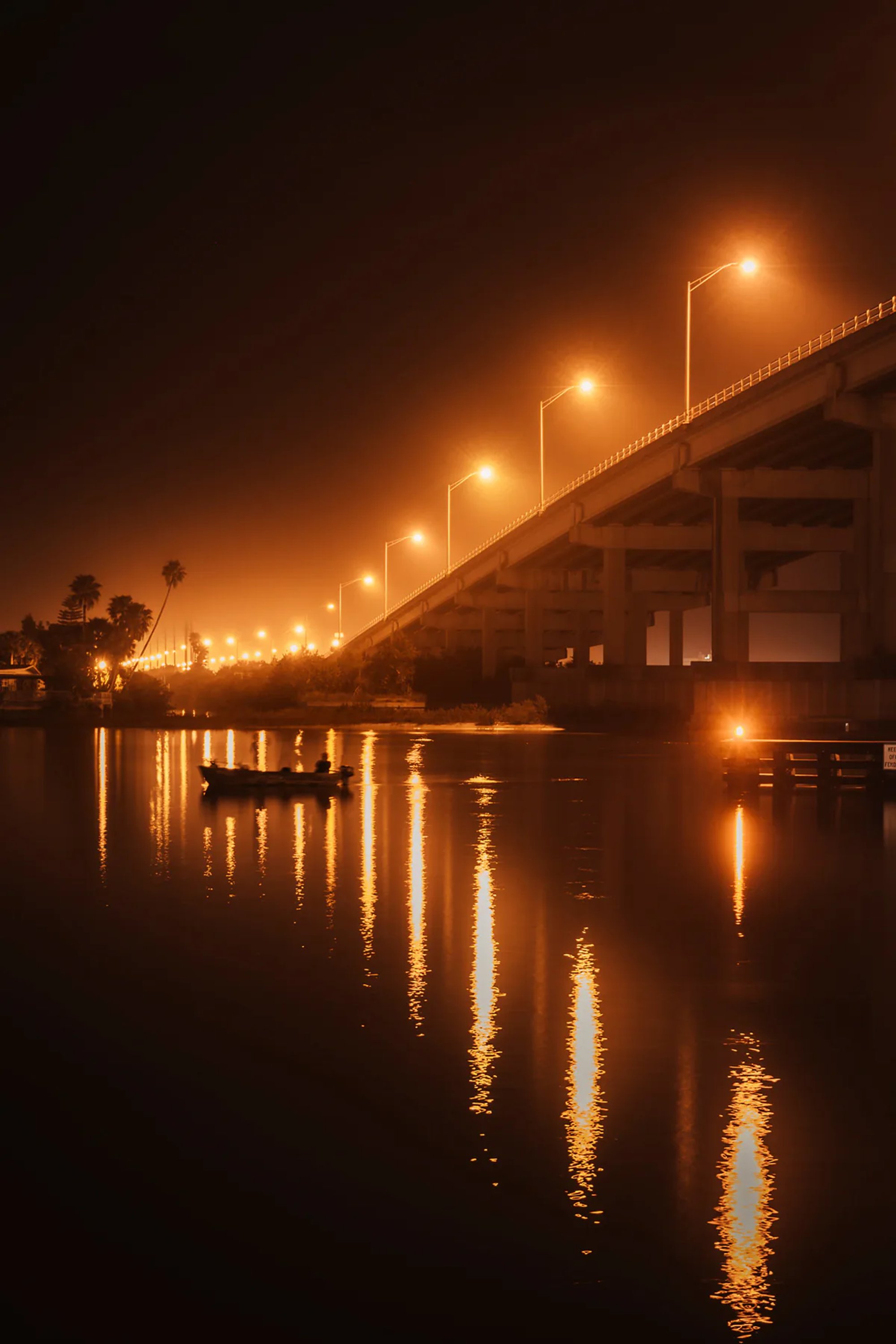 Bridge lights reflecting in calm water at night.