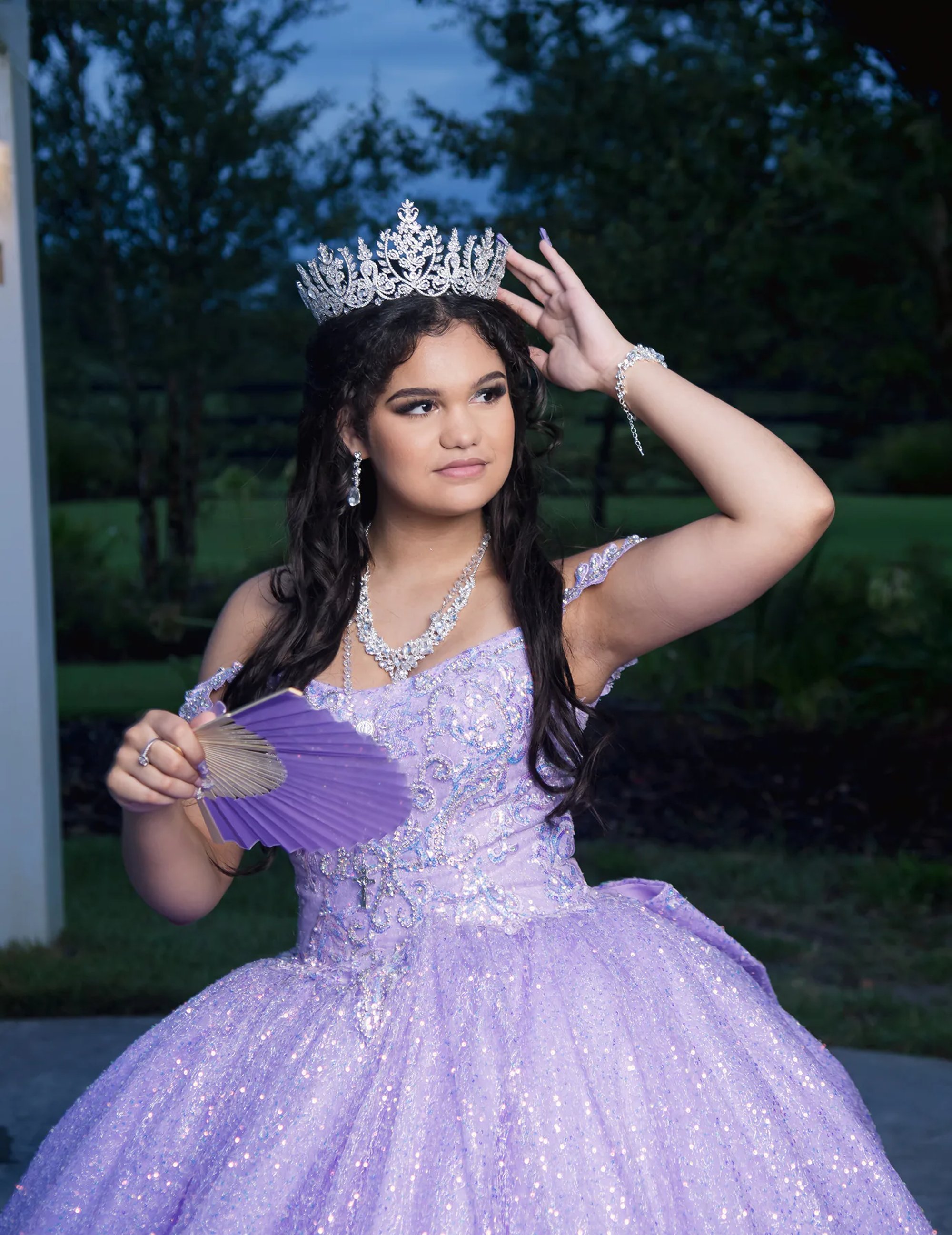 Quinceañera adjusting her tiara while holding a purple fan.