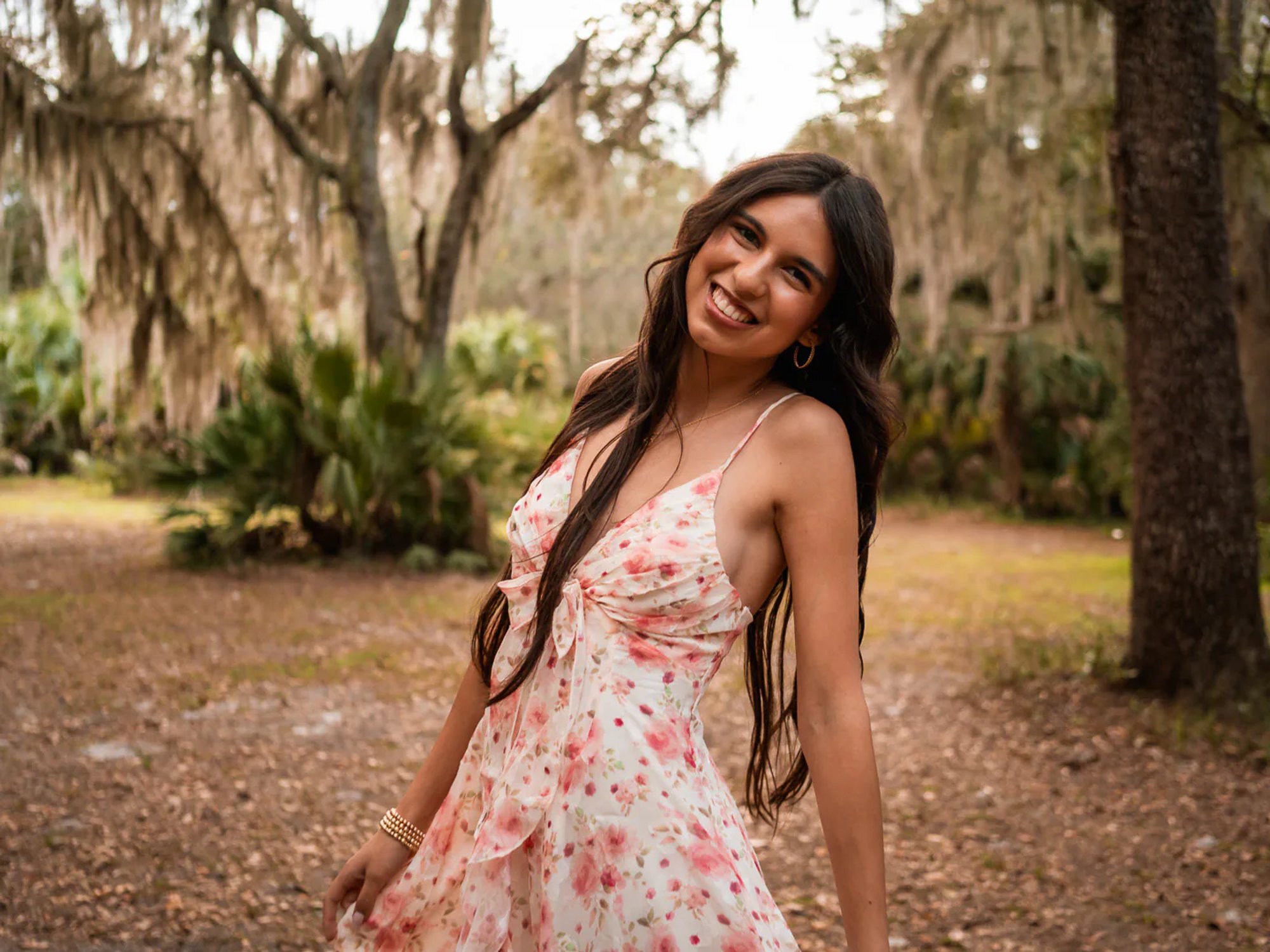 Young woman in a floral dress beneath trees draped with Spanish moss.
