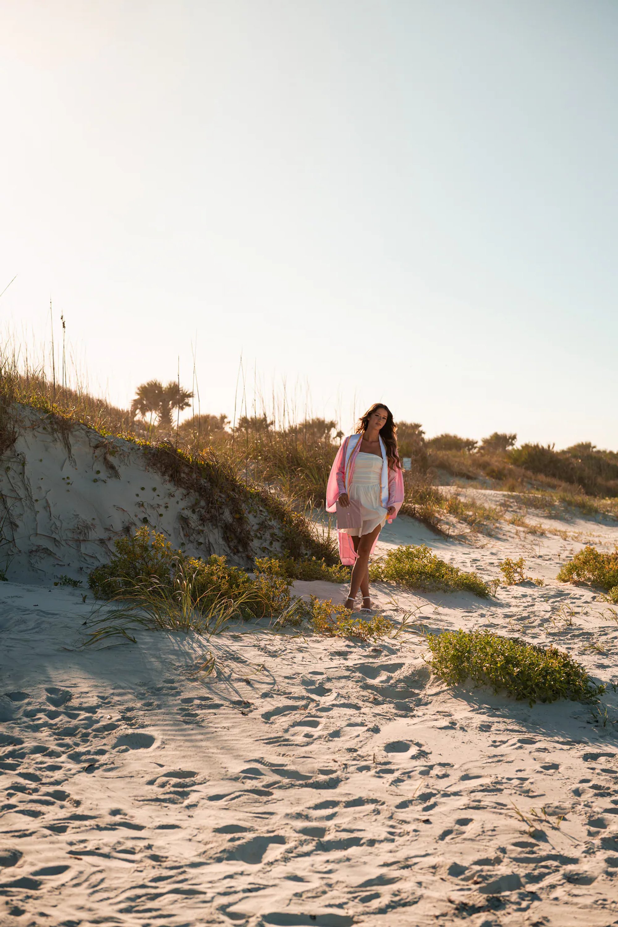 Young woman in a pink wrap standing on a sandy path through coastal dunes.