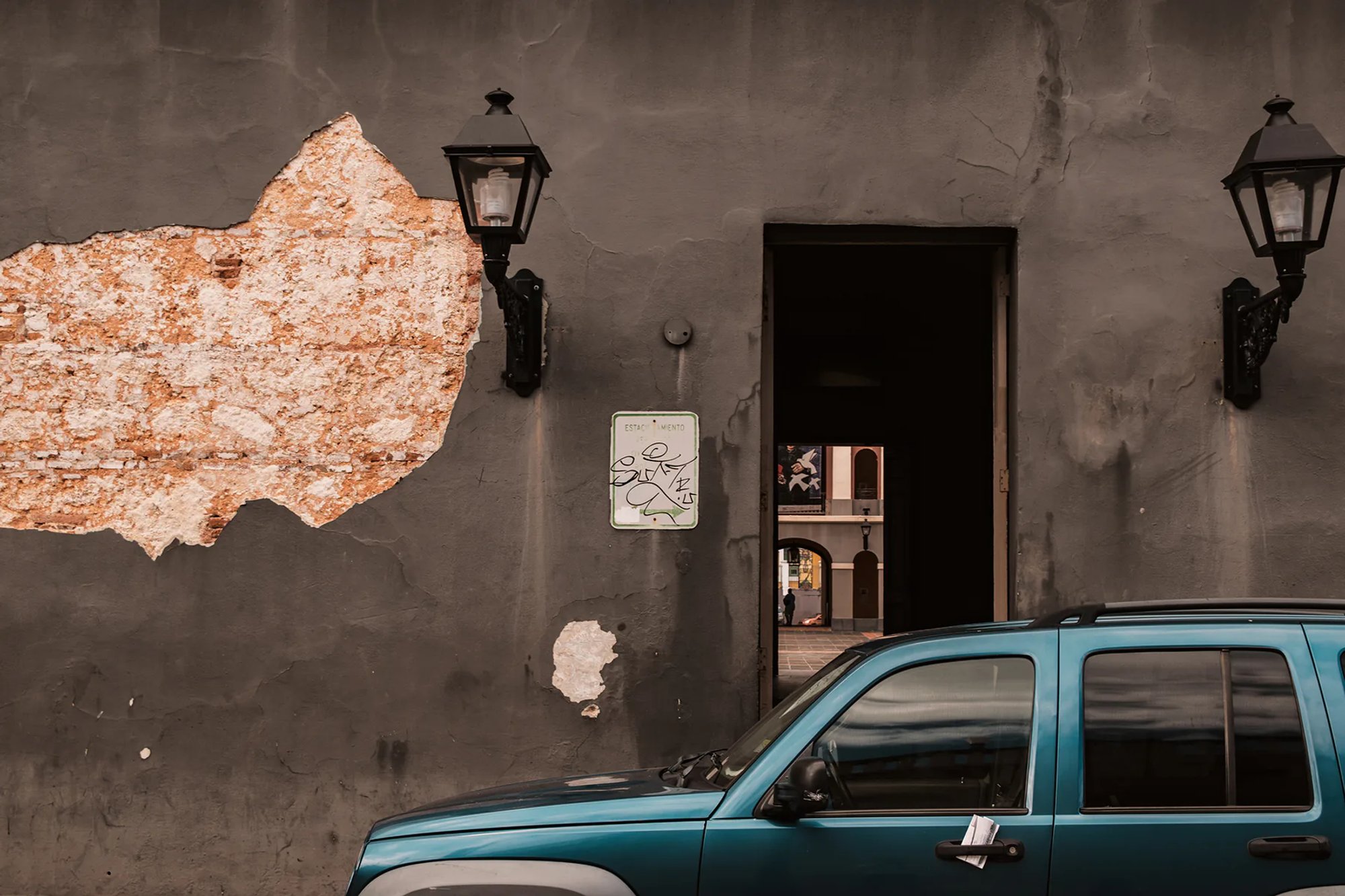 Blue pickup truck parked outside a weathered dark building.