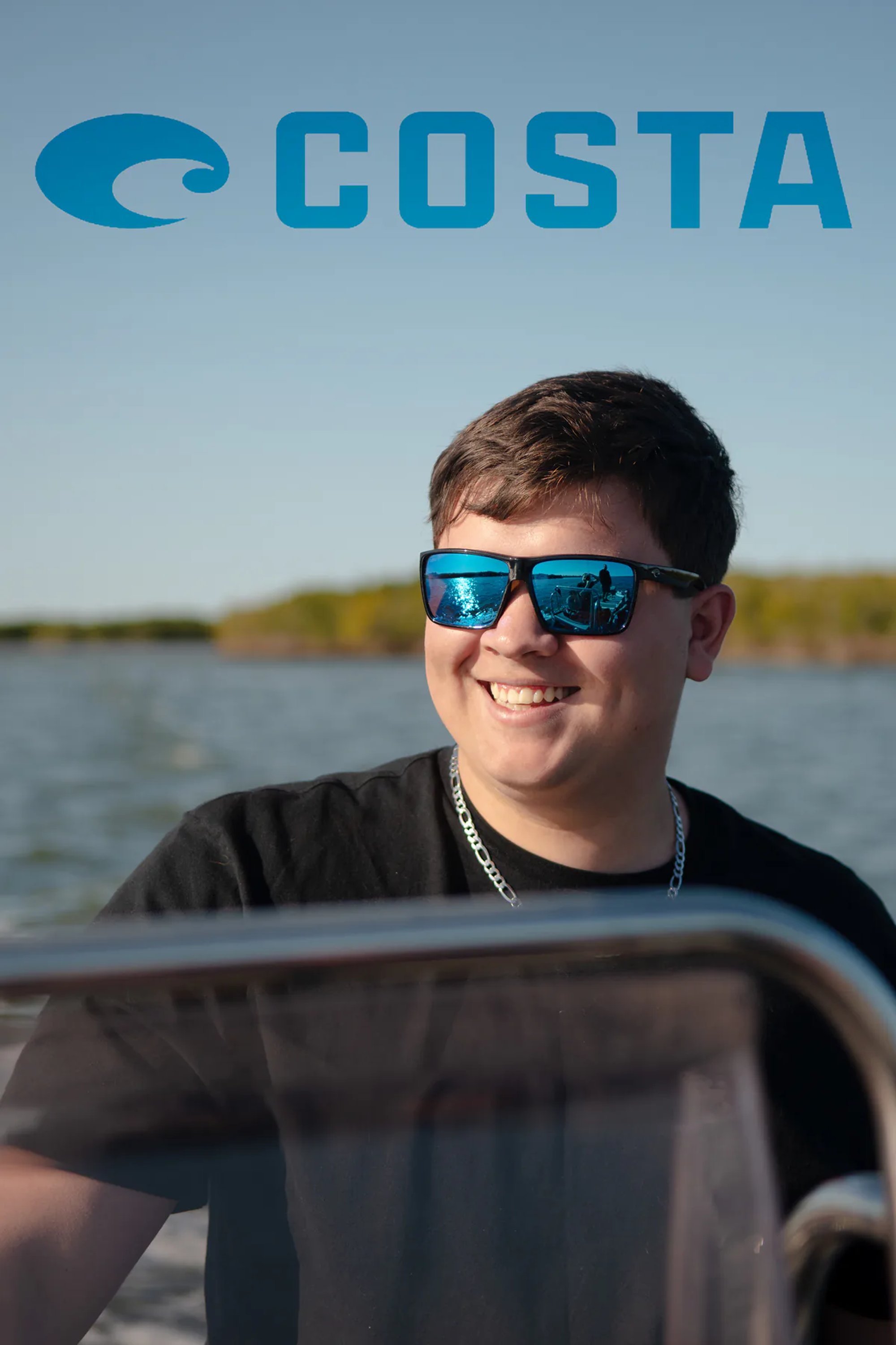 Person wearing blue sunglasses at a boat's wheel beneath a Costa logo.