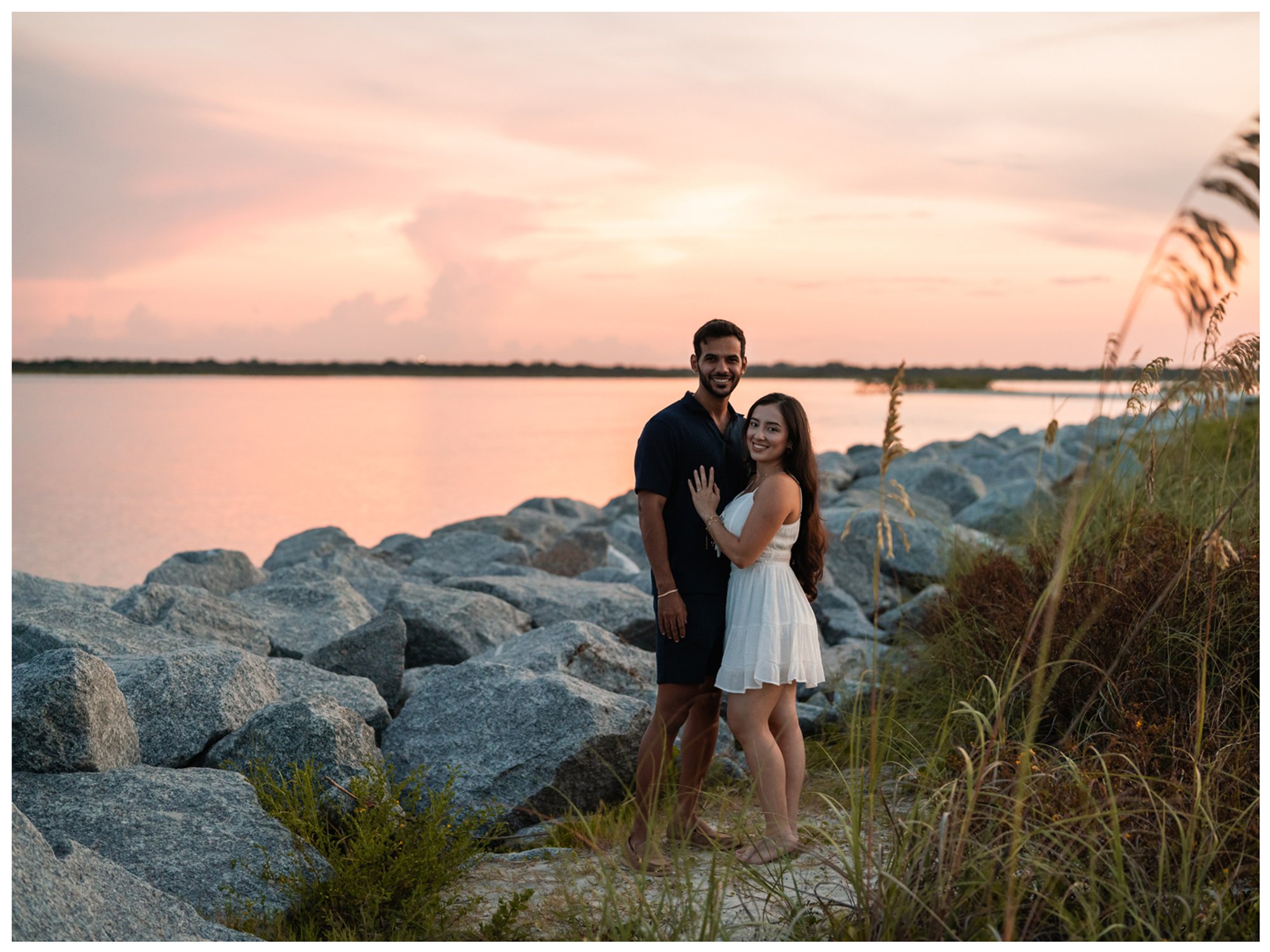 Dierick and Paulina beside the inlet rocks beneath a soft pink sunset.