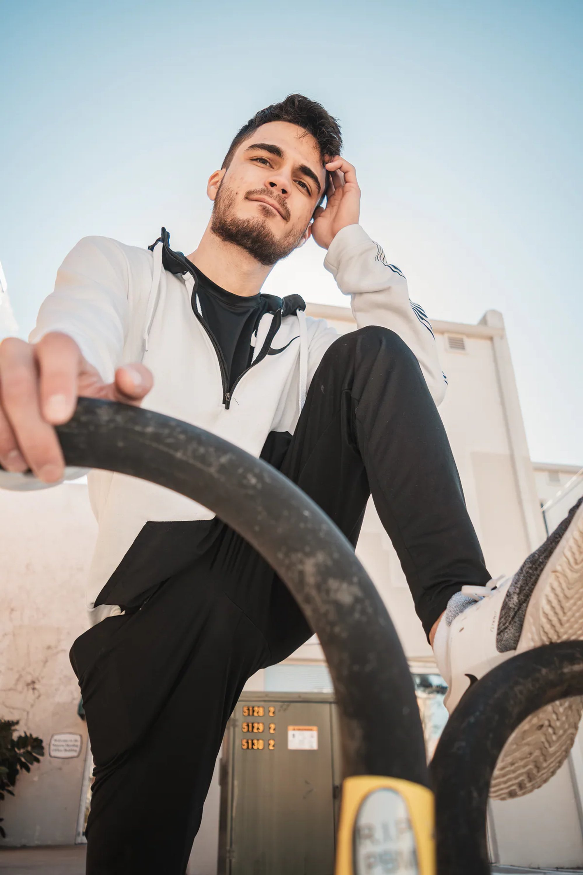 Low-angle portrait of a man in a white hoodie on outdoor exercise equipment.
