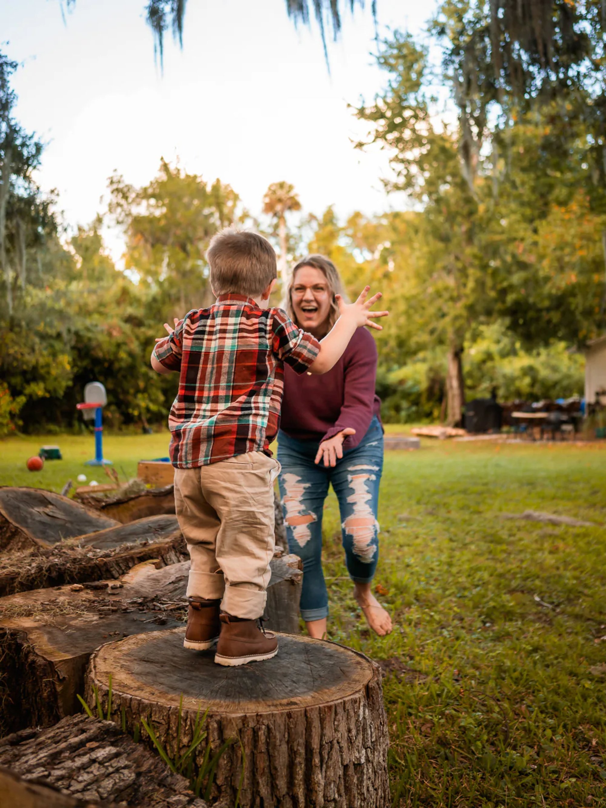 Mother playing with her son as he jumps off a tree stump in their backyard in New Smyrna Beach, Florida.