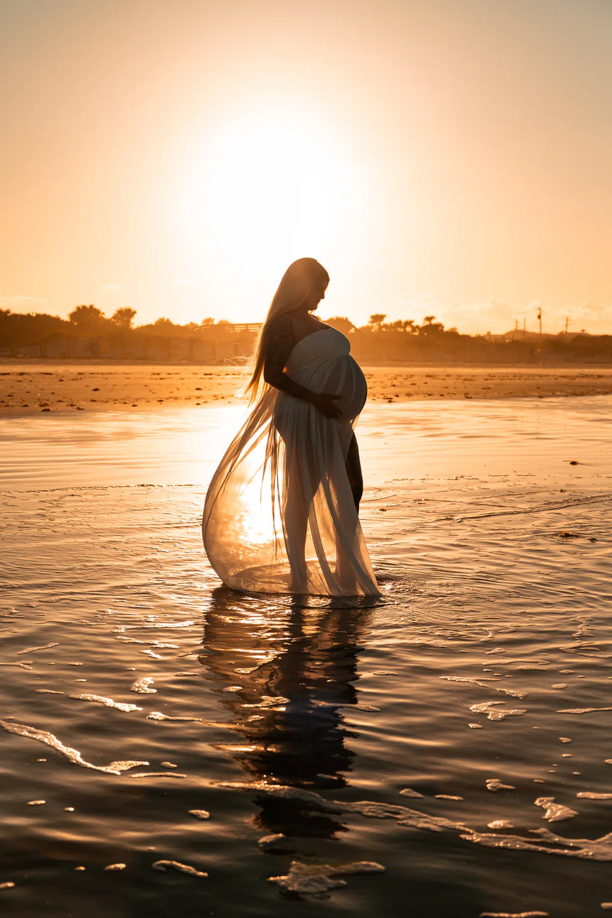 Silhouette maternity photo of pregnant mother standing in the water at sunset