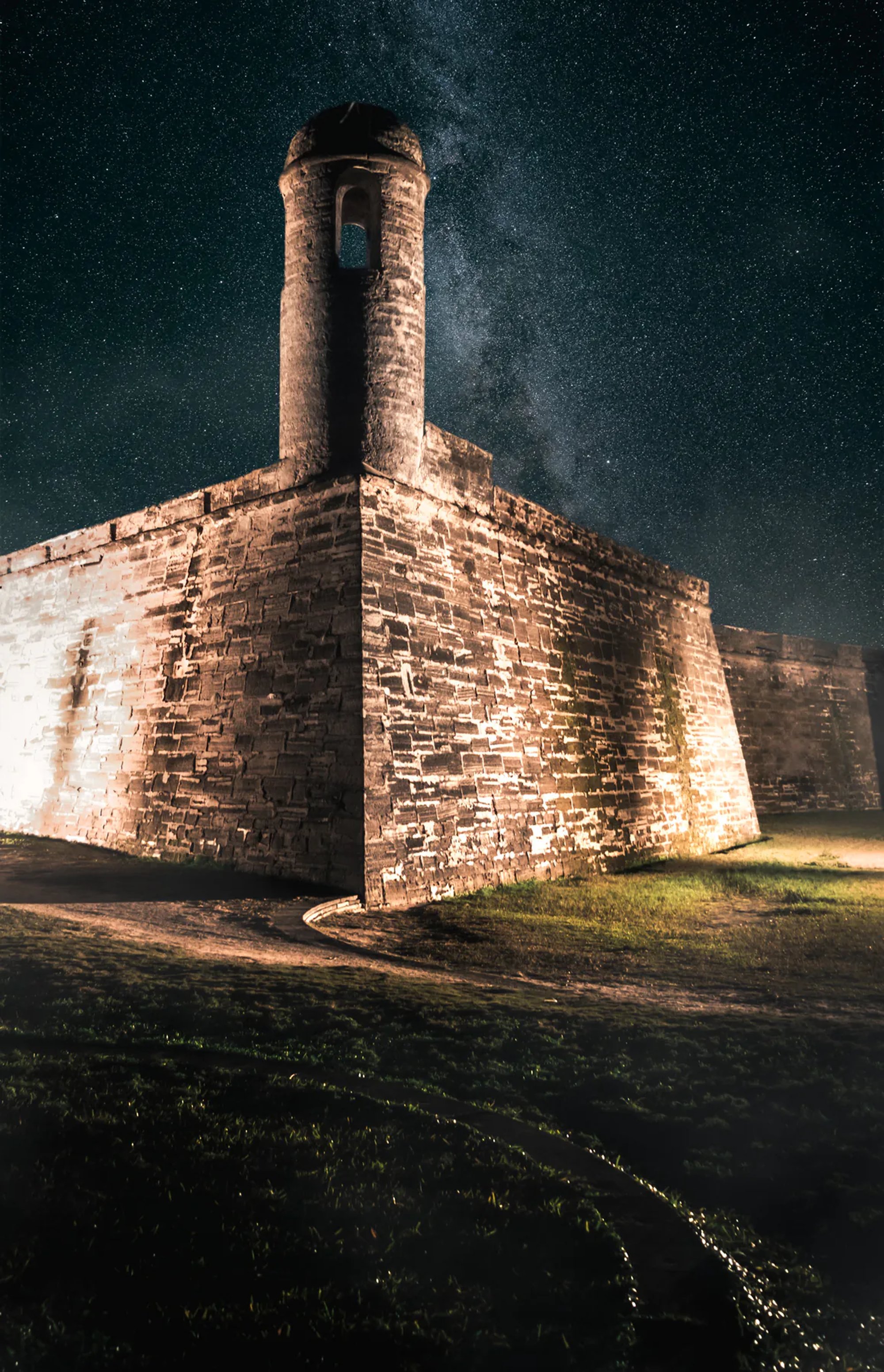 Stone chimney and historic masonry wall illuminated at night.