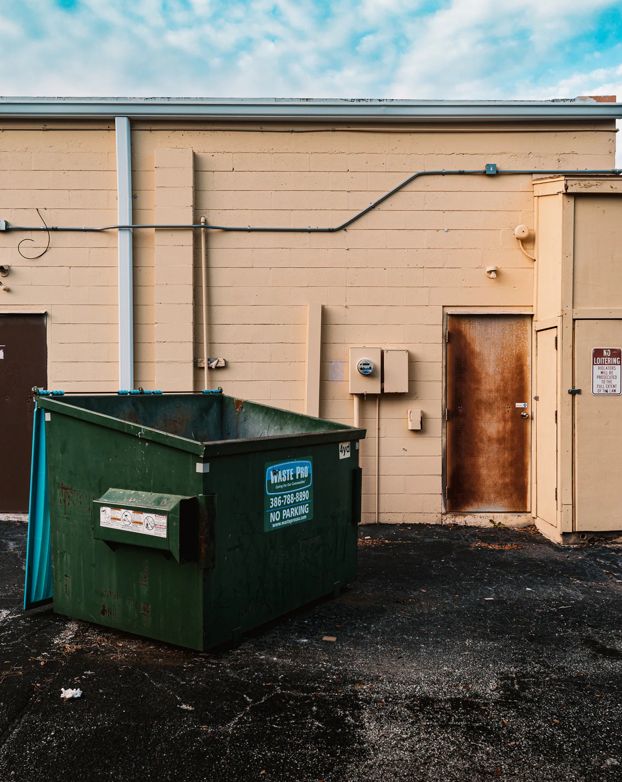 Green dumpster behind a beige industrial building.