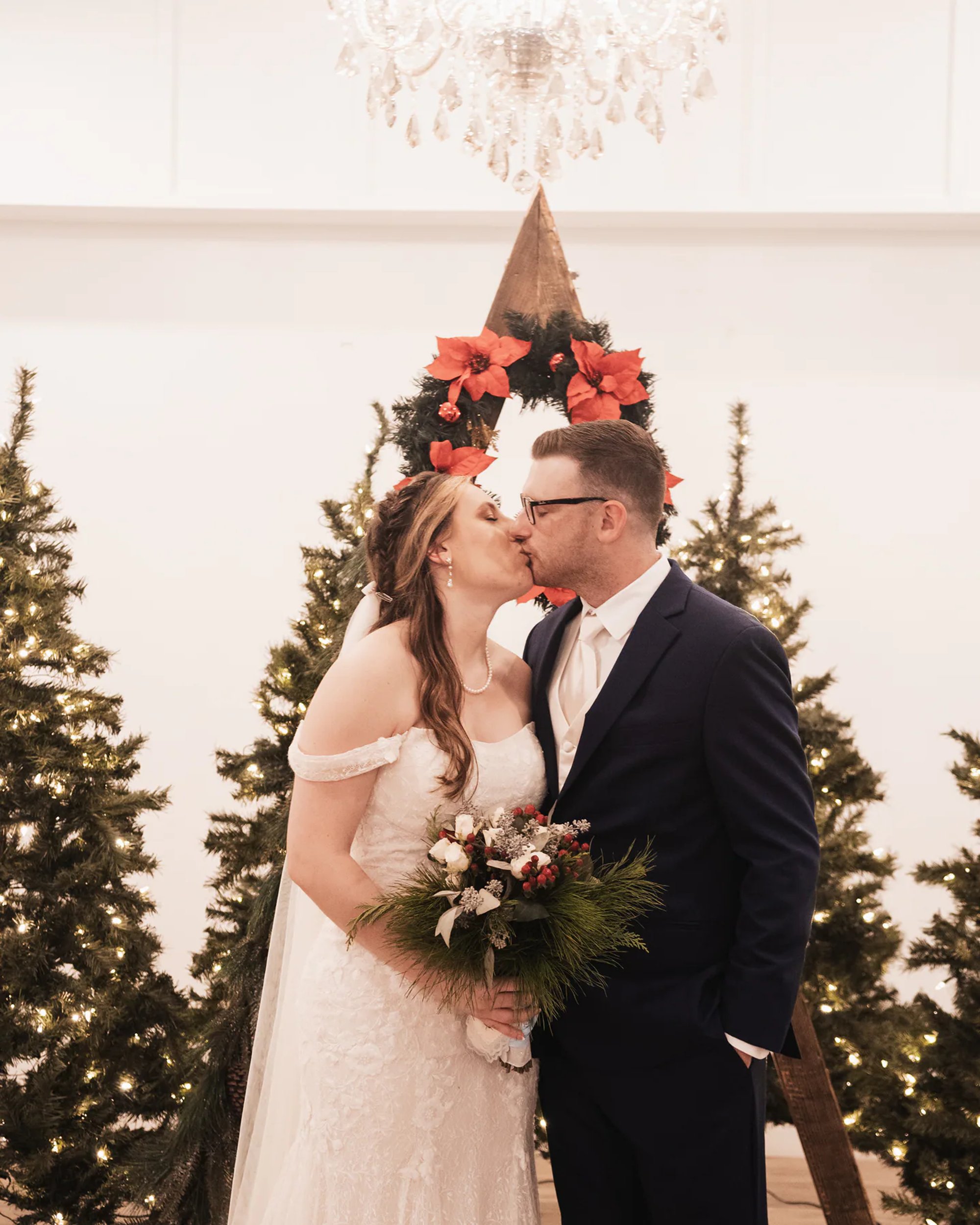 Newlyweds kissing in front of decorated Christmas trees.