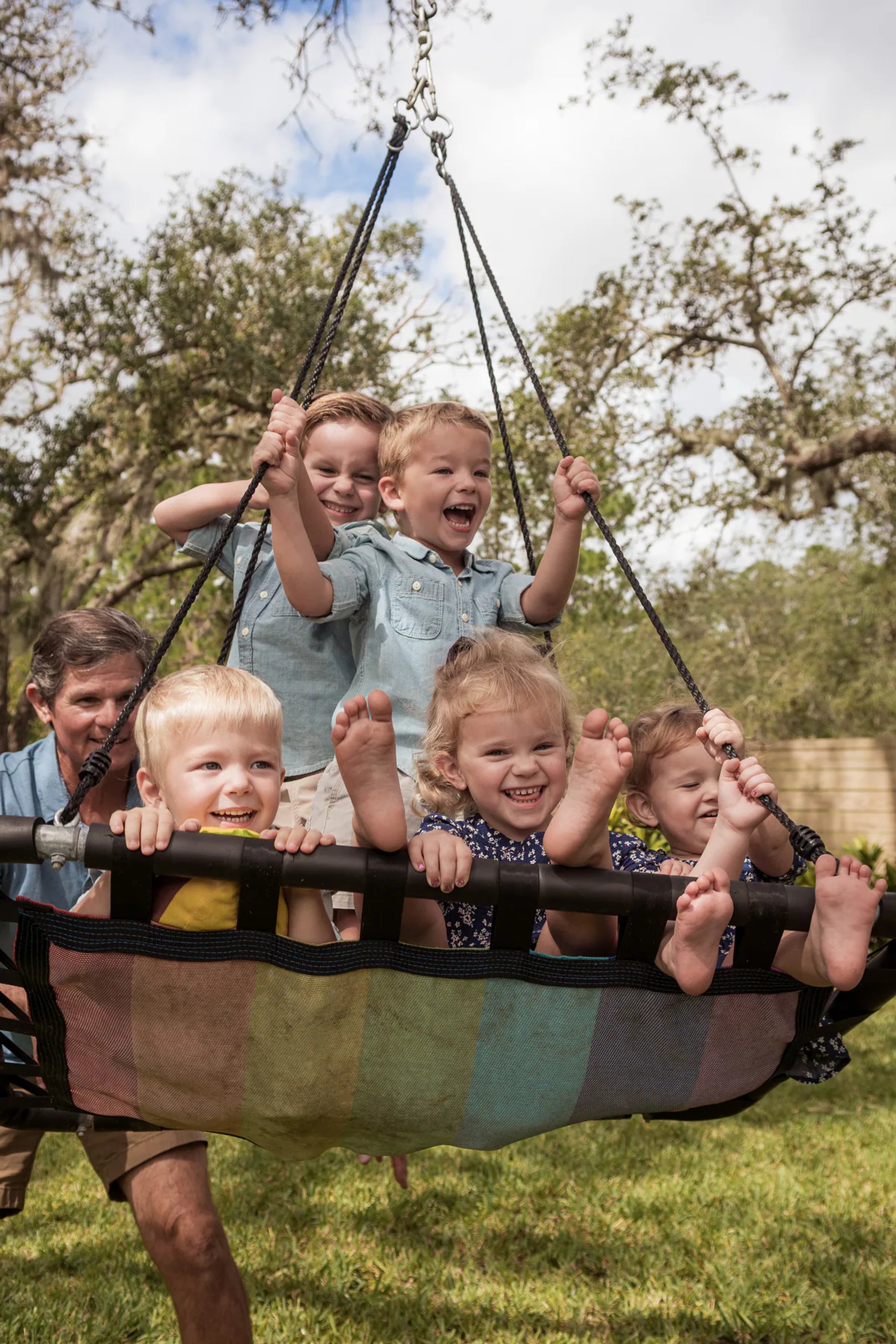Adults lifting a large swing filled with smiling children.
