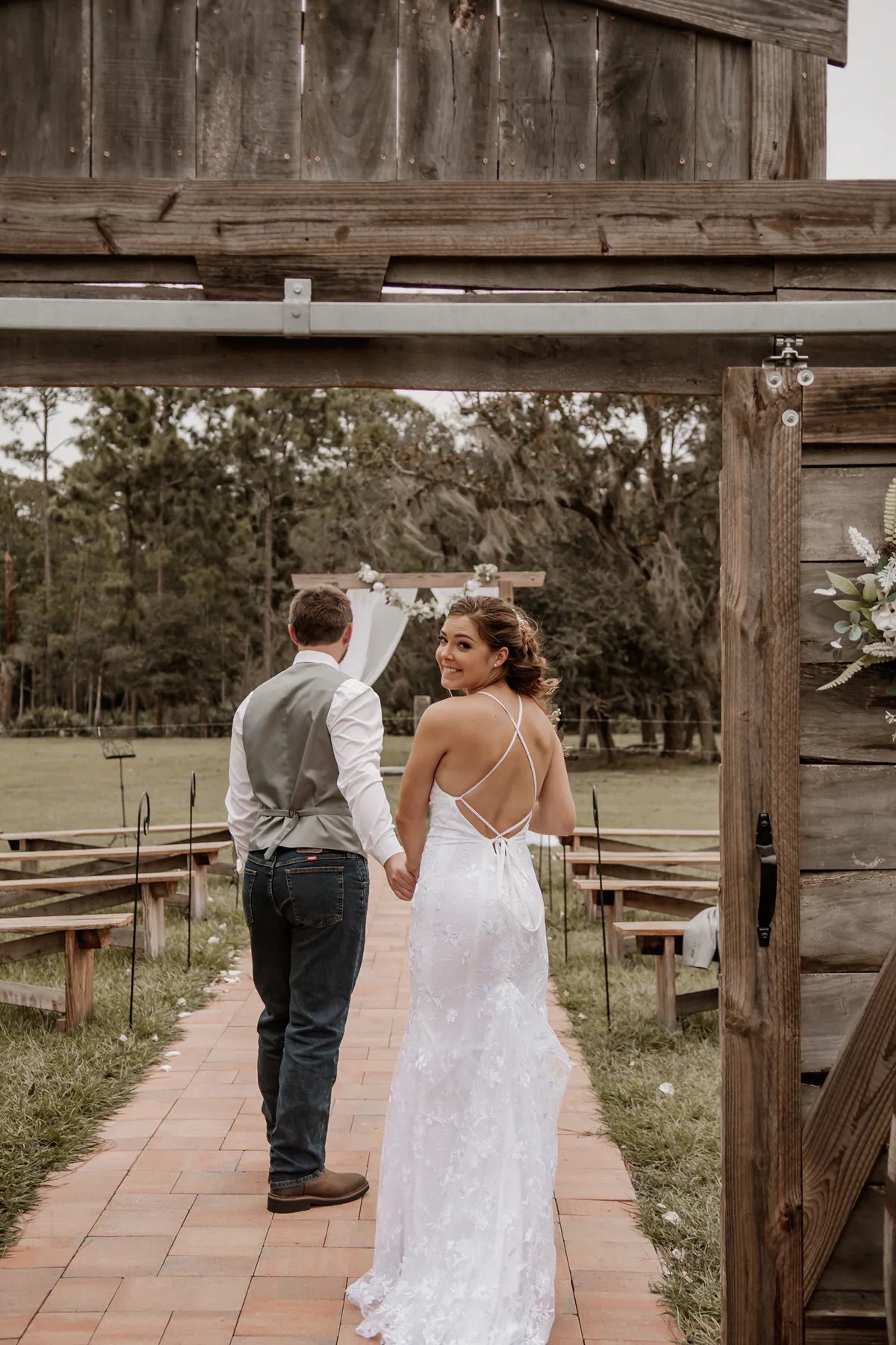 Newlyweds walking away together through a rustic wooden entrance.