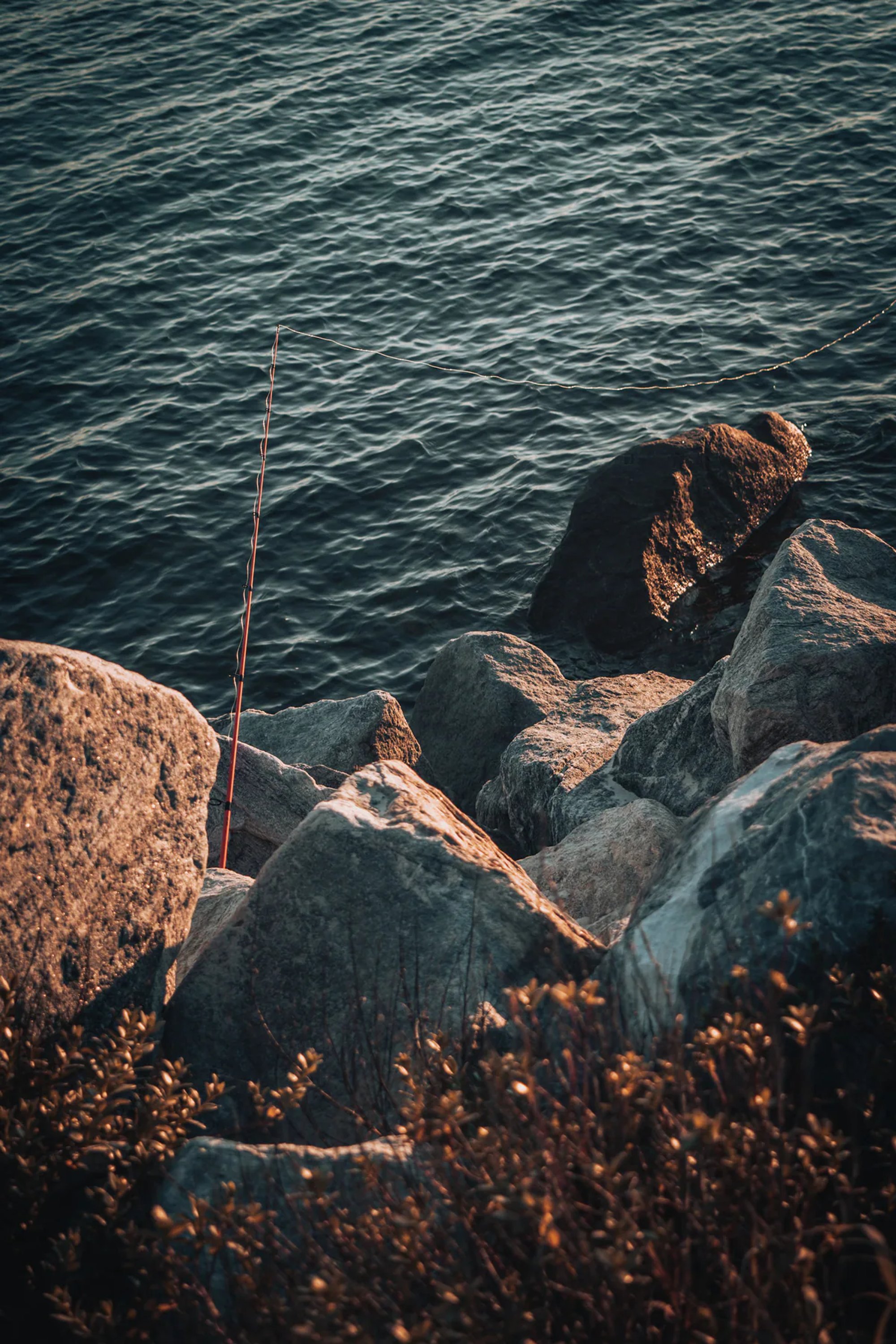 Person seated on shoreline rocks beside dark ocean water.