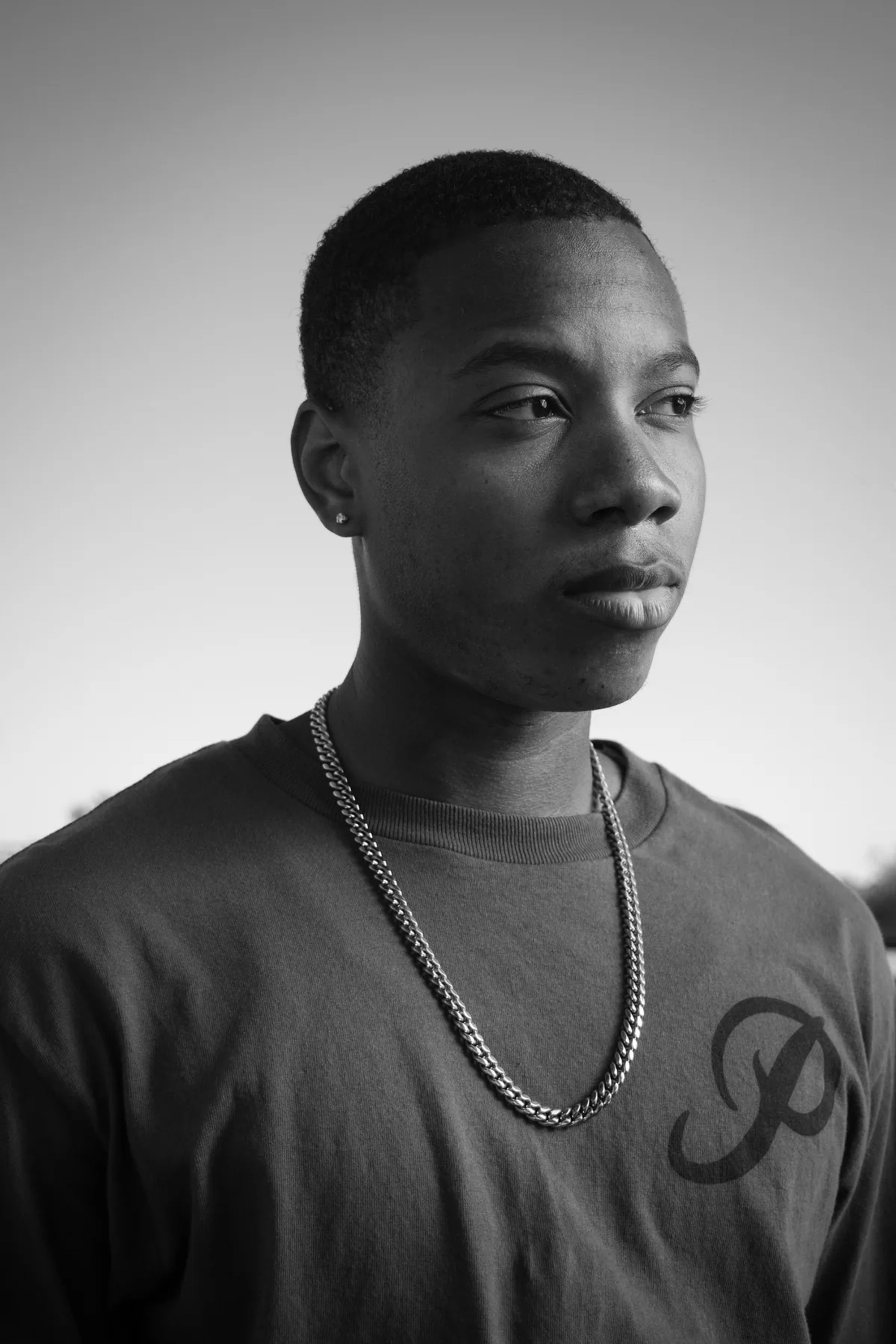 Black-and-white close portrait of a young man wearing a chain necklace.