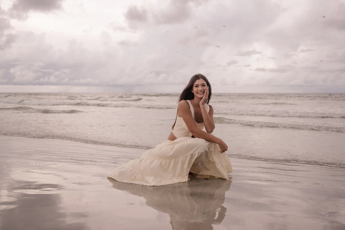 Senior portraits on Ponce Inlet Beach with Mia sitting on the shoreline in a cream dress, natural light photography in Daytona Beach FL.
