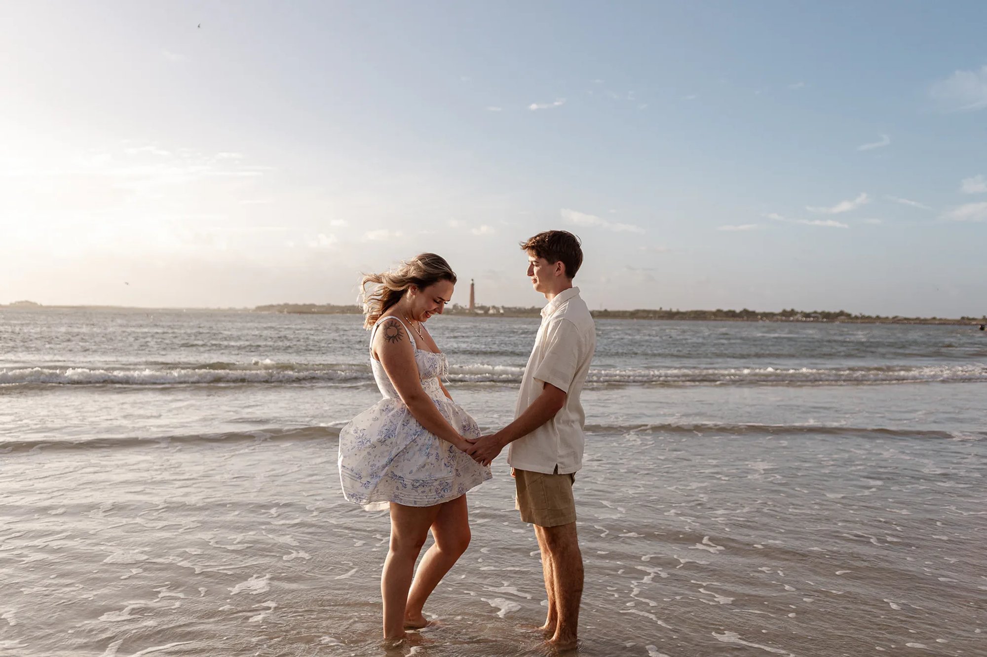 Engagement photos on the beach, Joey and Lexi smiling and holding hands in shallow ocean water.