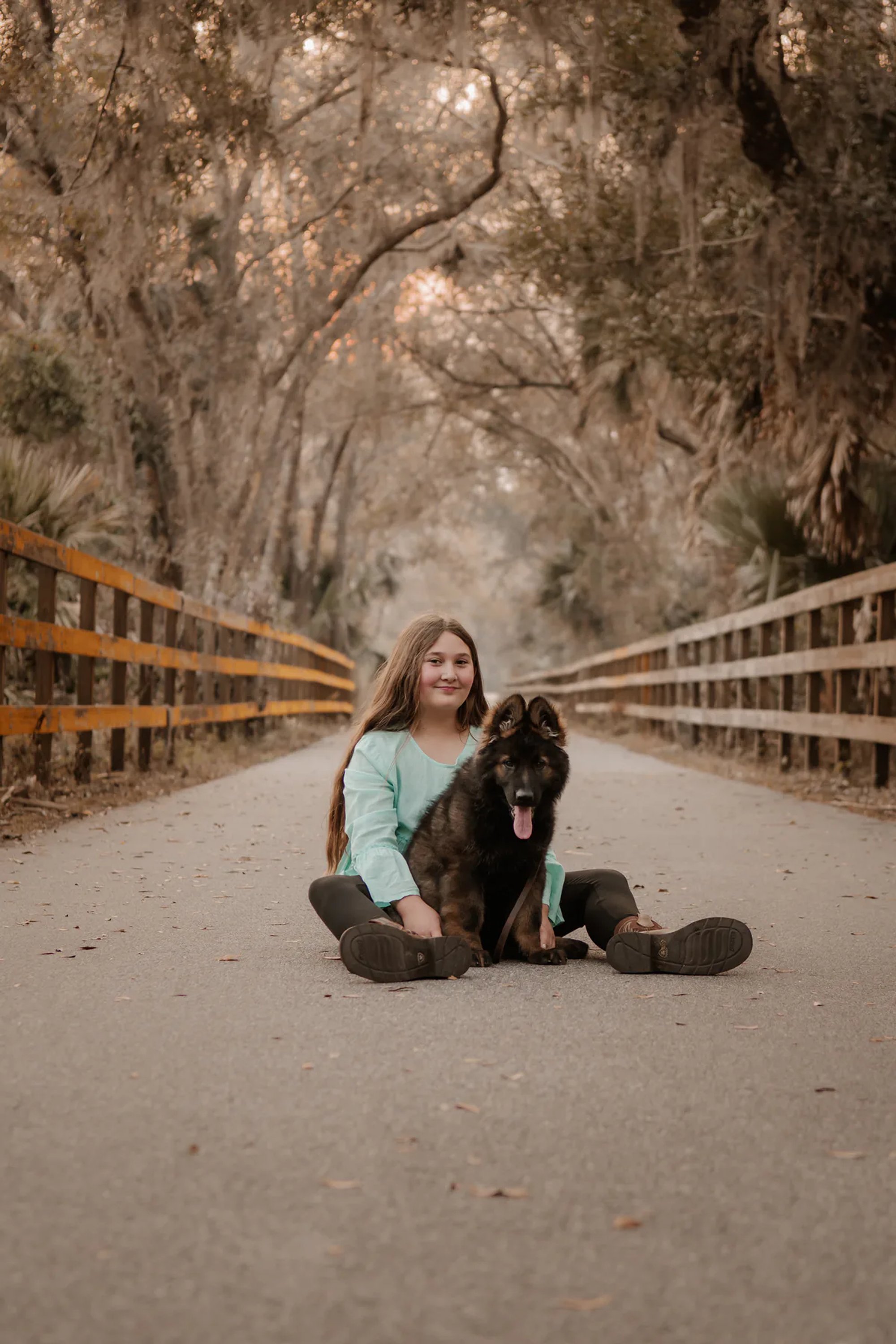 Young woman sitting with her black dog in the middle of a quiet road.