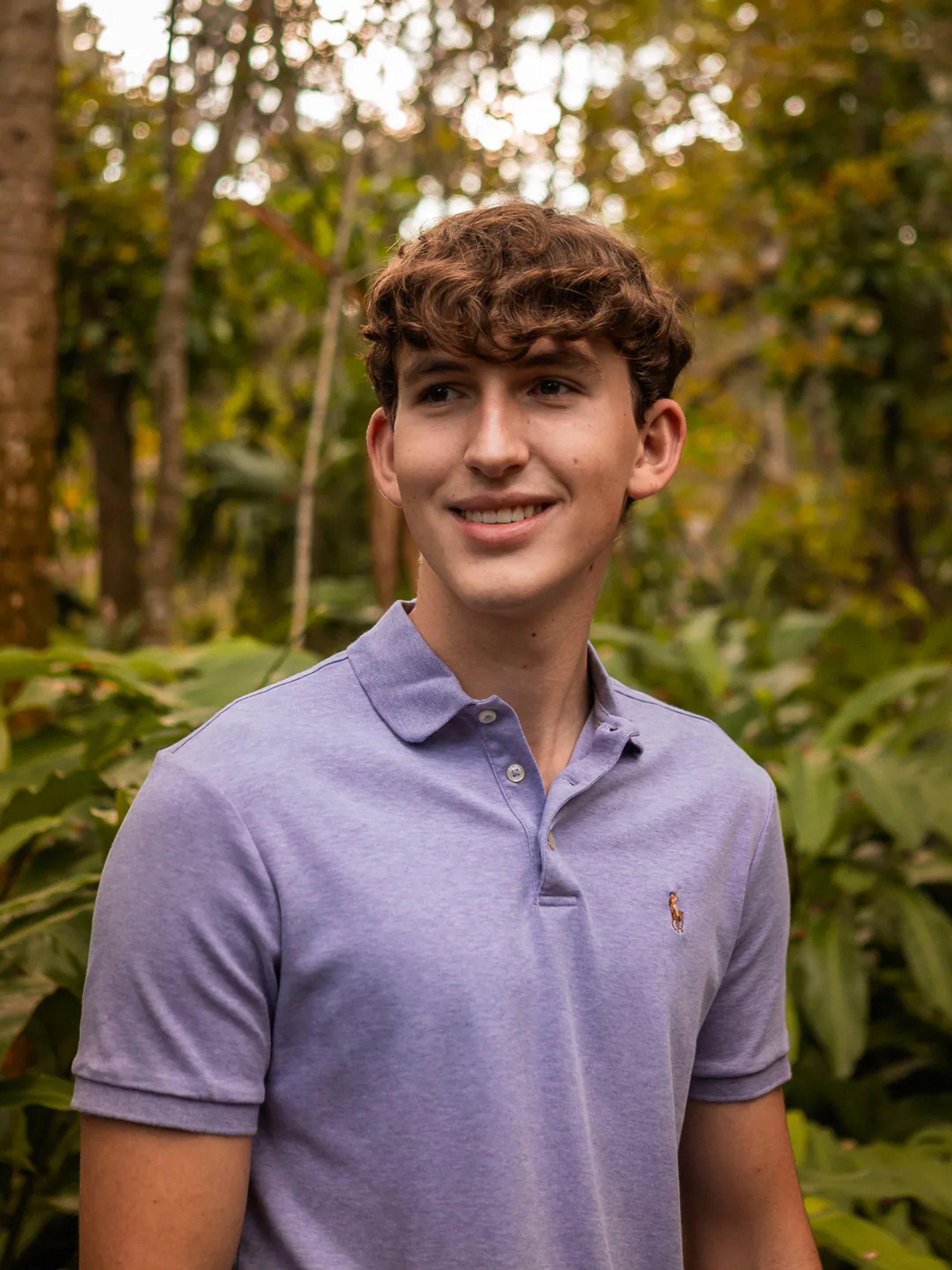 Young man in a purple polo shirt surrounded by greenery.