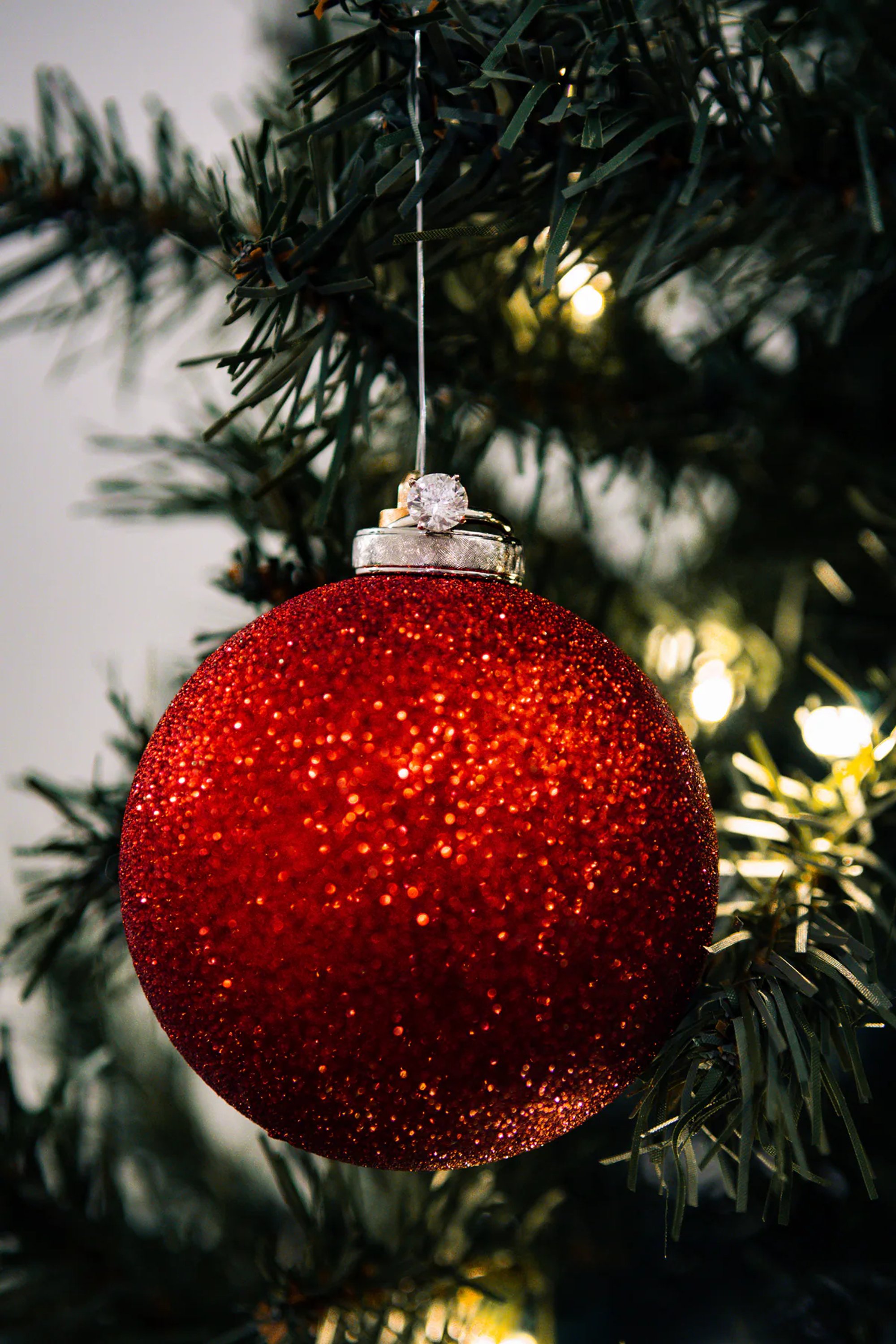 Red glitter Christmas ornament hanging from an evergreen branch.