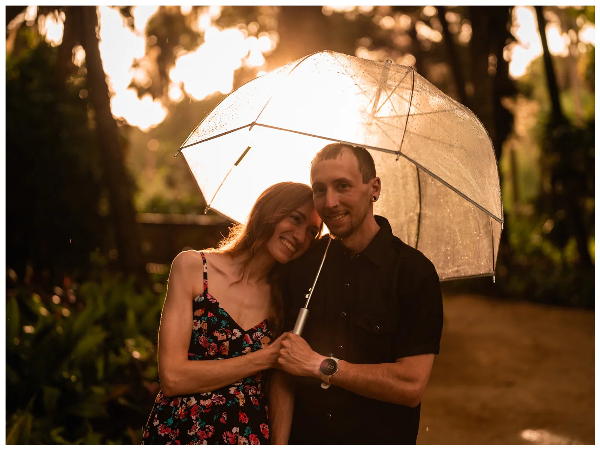 Smiling couple standing close together beneath a clear umbrella at Washington Oaks Gardens.