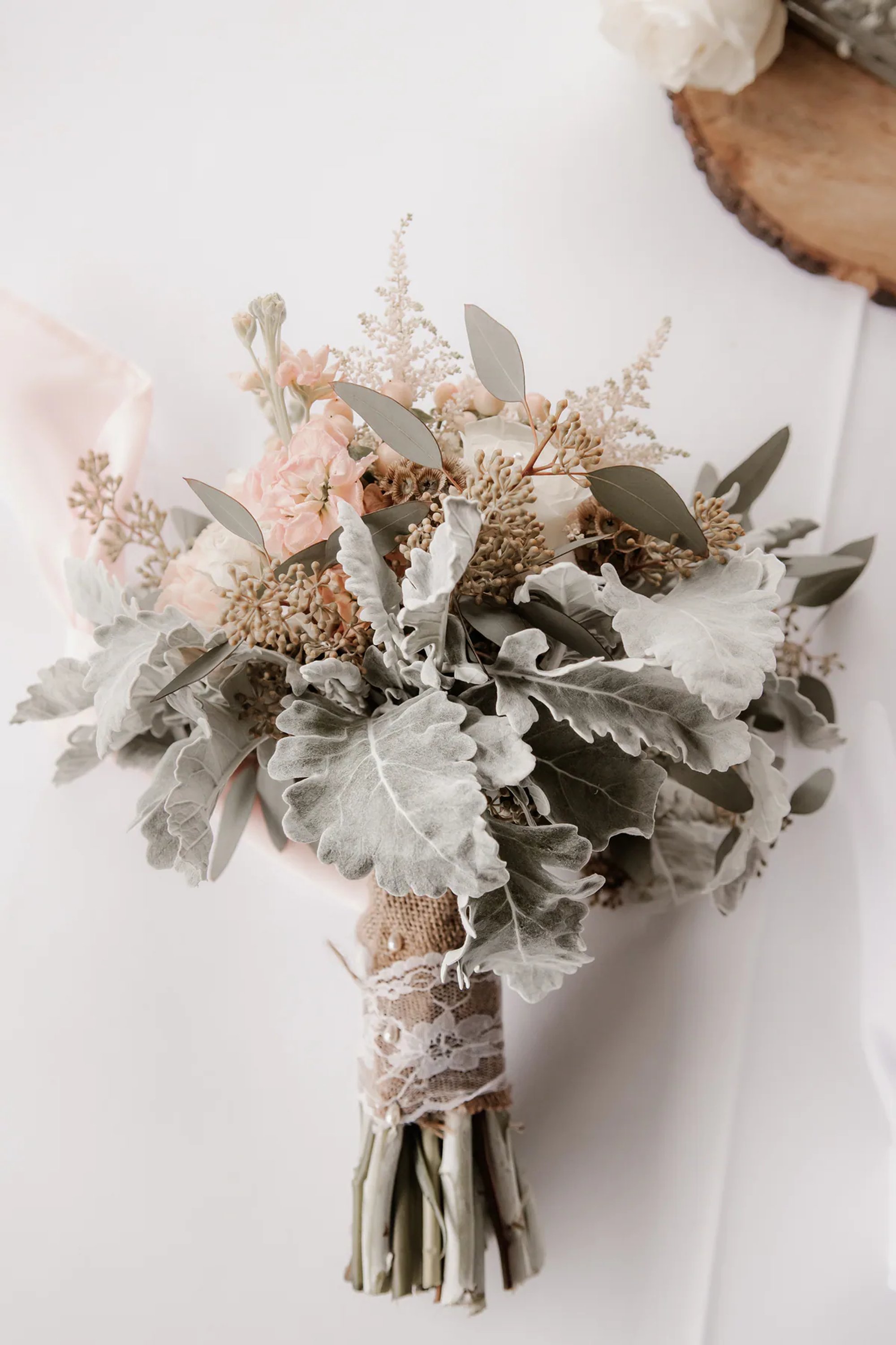 Neutral wedding bouquet of white flowers and greenery resting on a light surface.