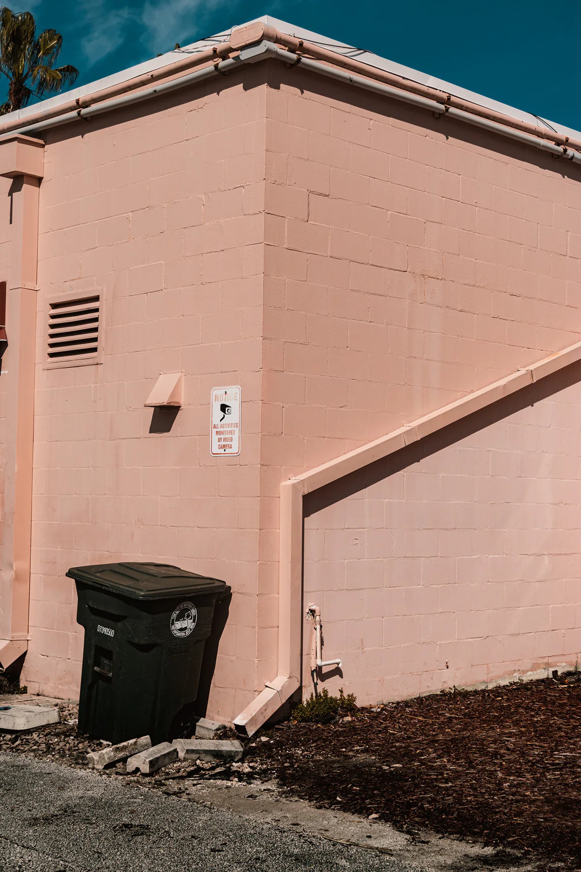 Pale pink building corner with a black dumpster beside a sloped wall.