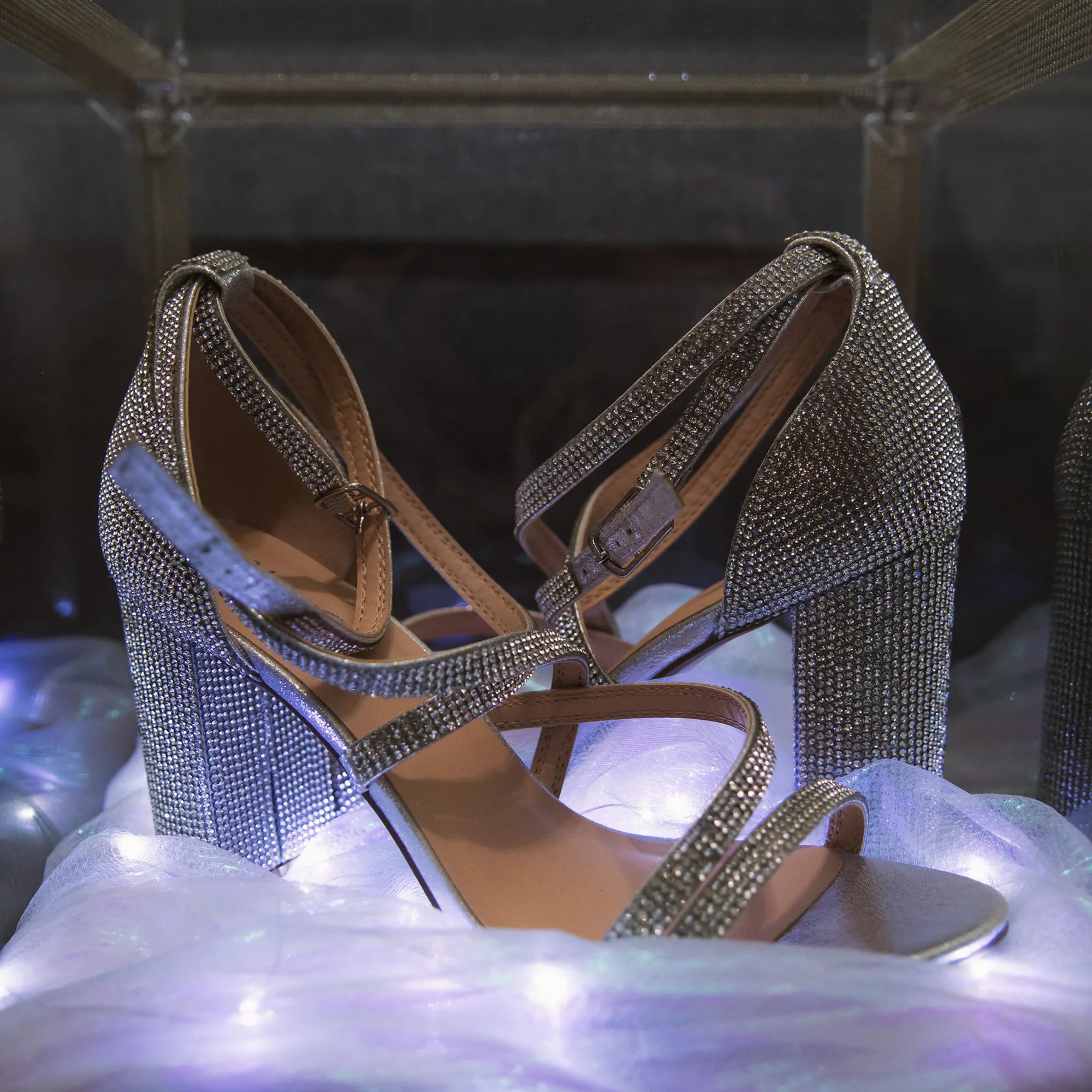 Sparkling silver high heels arranged on illuminated fabric.