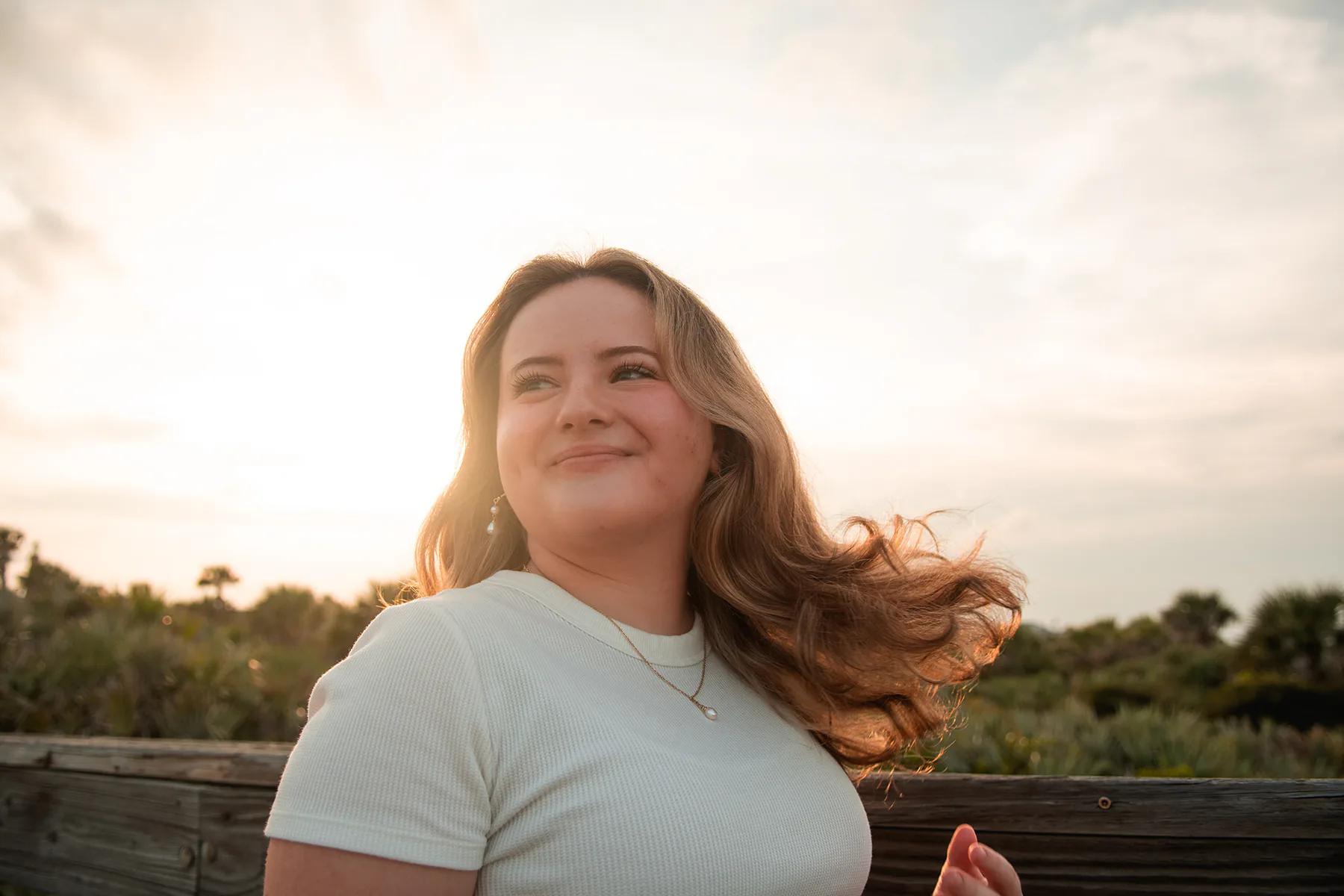 Young woman in warm sunset light near a beach boardwalk.