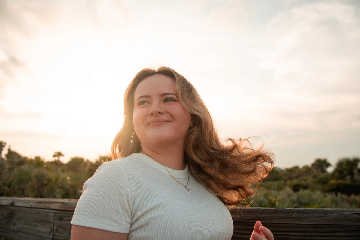 Young woman in warm sunset light near a beach boardwalk.