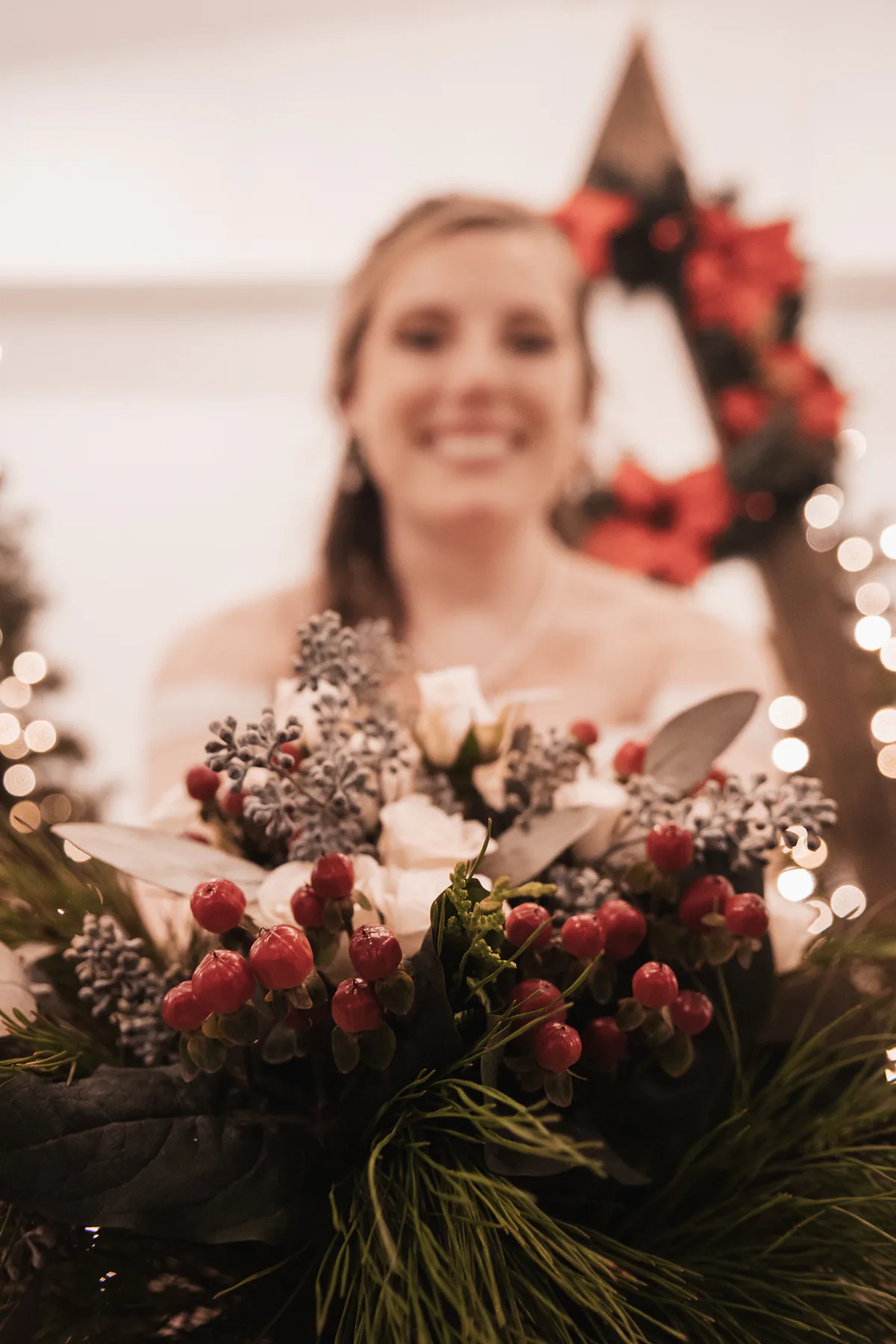 Smiling bride holding a deep red wedding bouquet beside Christmas decorations.