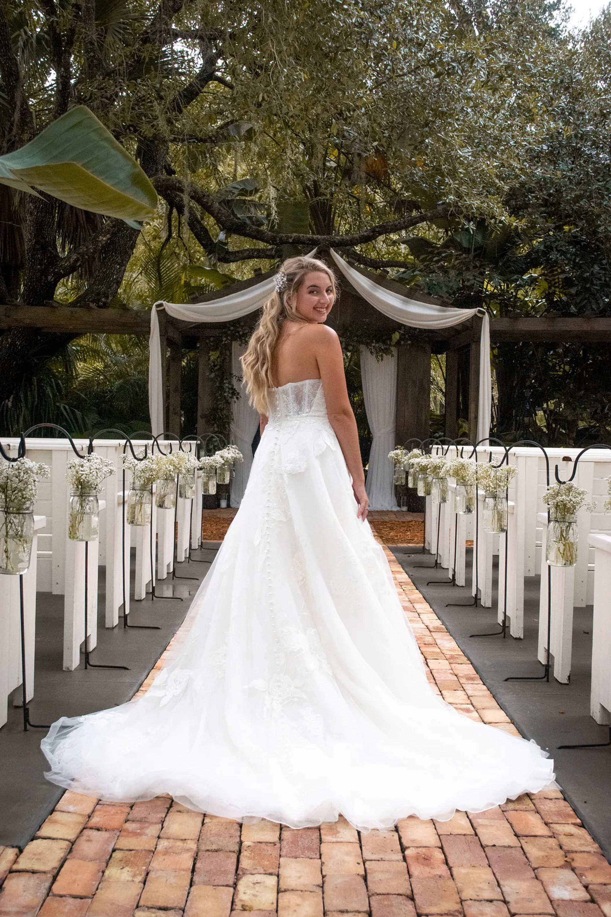 Bride walking down an outdoor ceremony aisle with a long train.