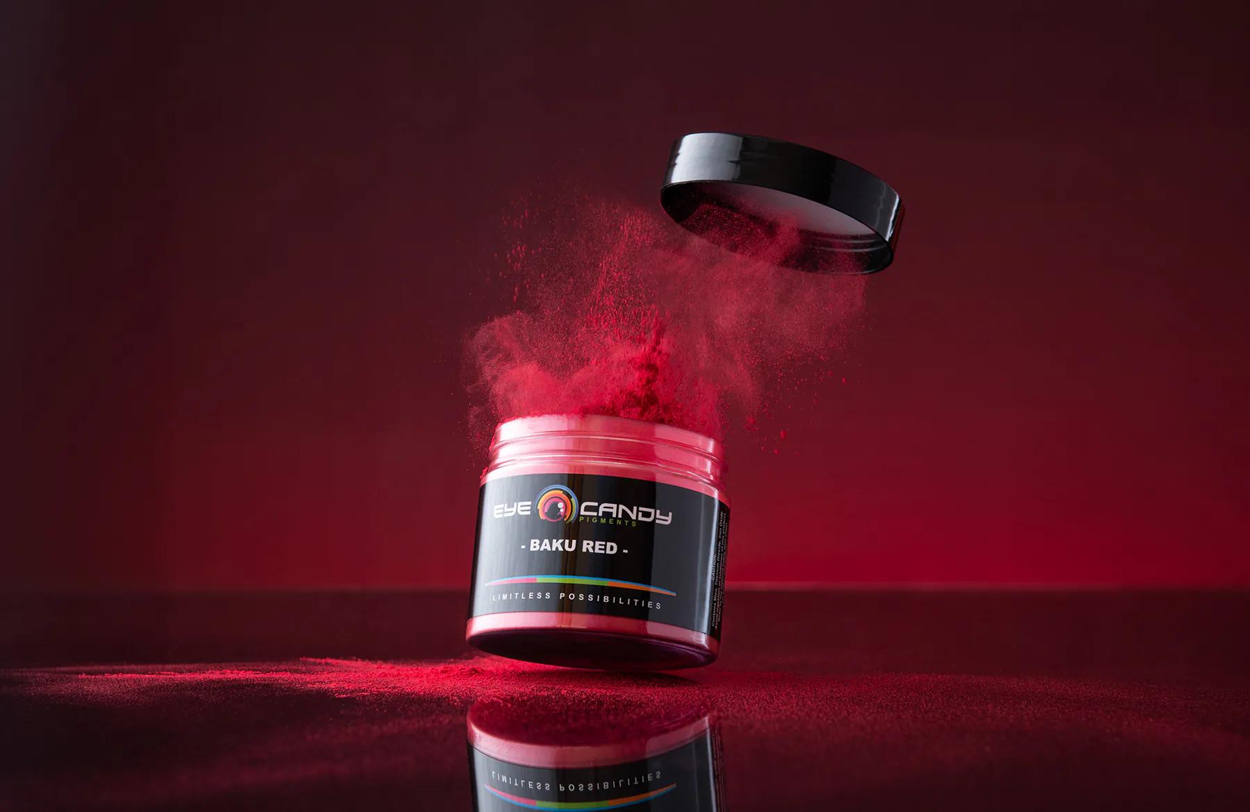 Eye Candy Pigments jar with red powder suspended above it on a red background.
