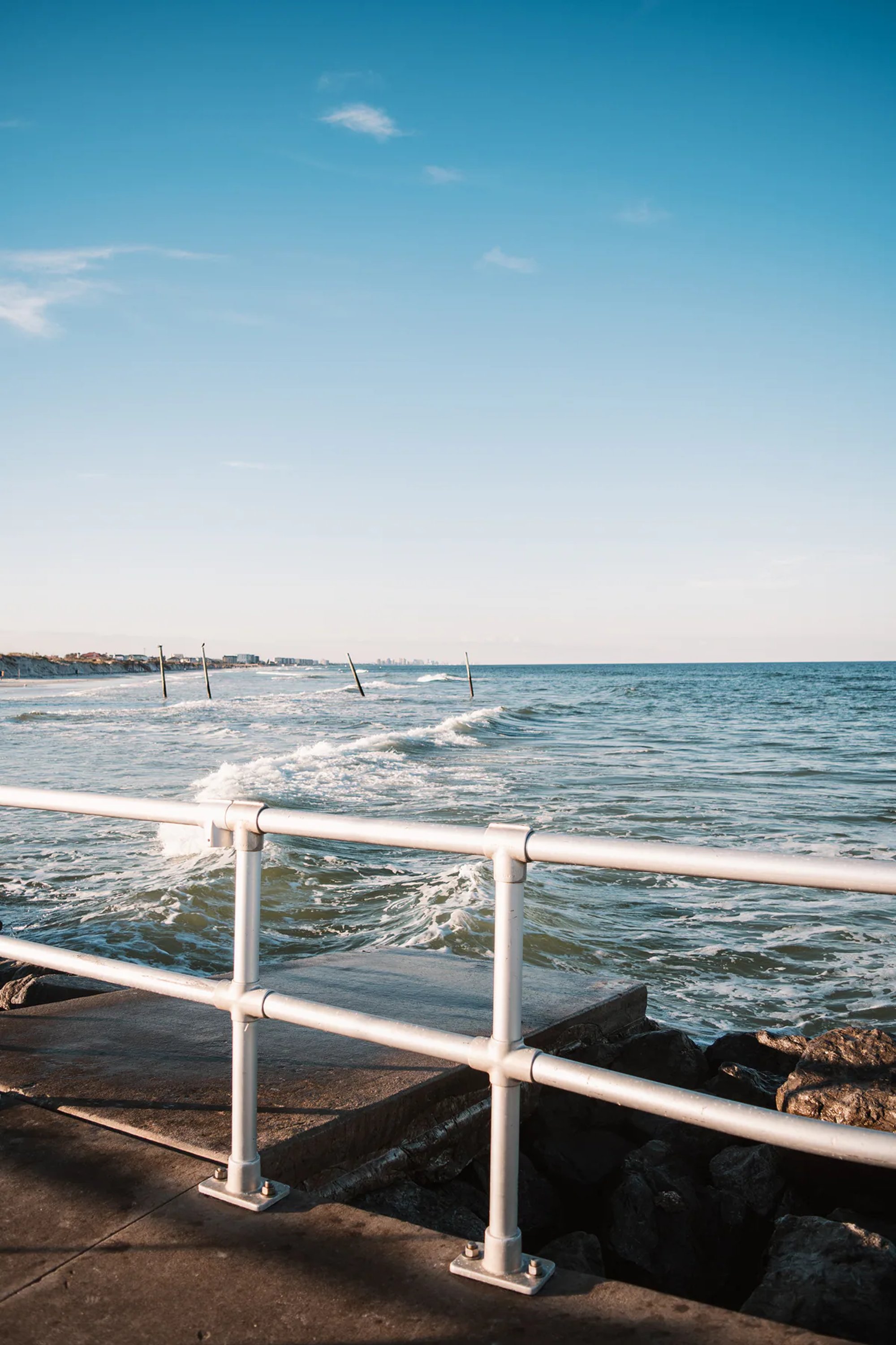 White railing beside waves breaking over coastal rocks.