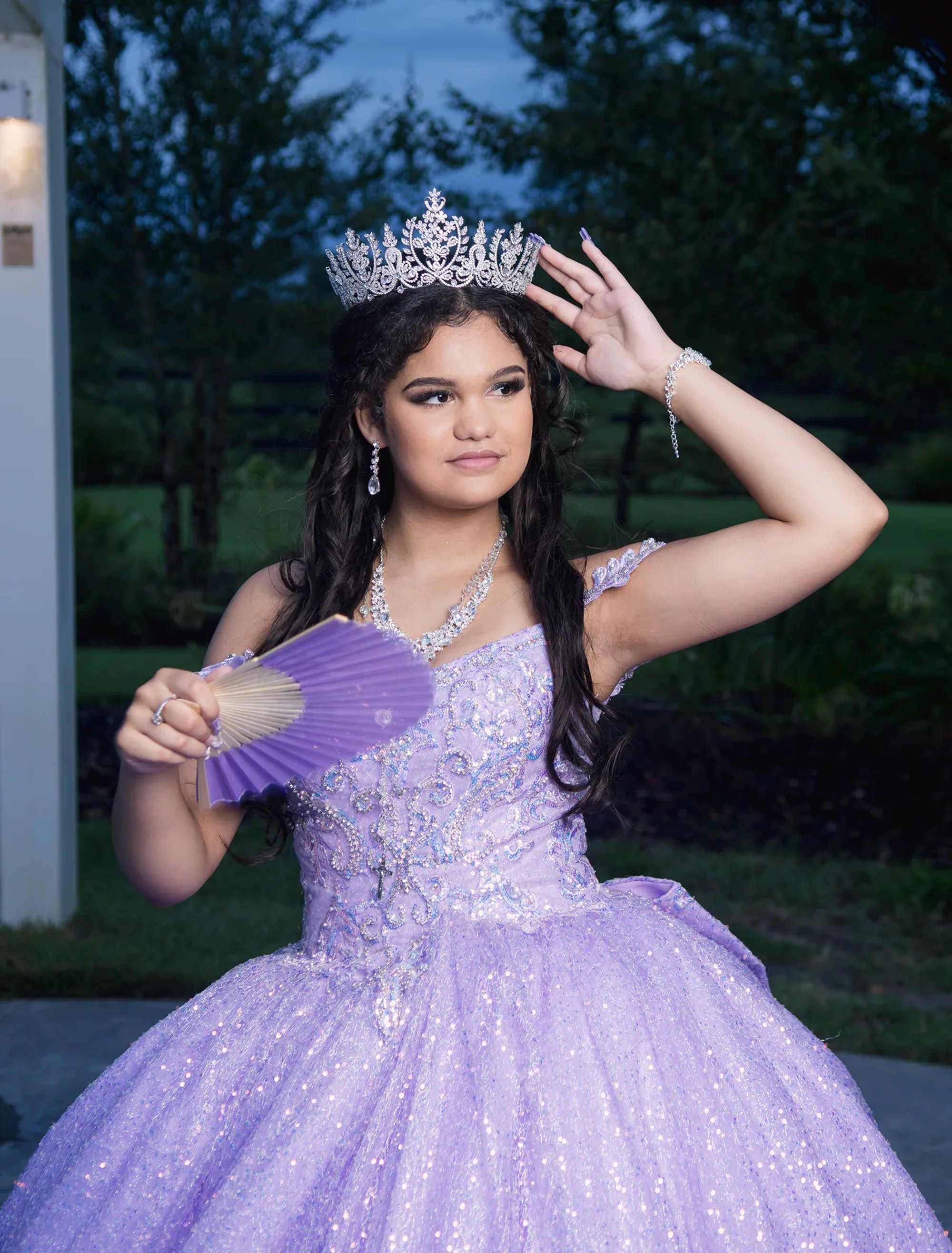 Quinceañera adjusting her tiara while holding a purple fan.