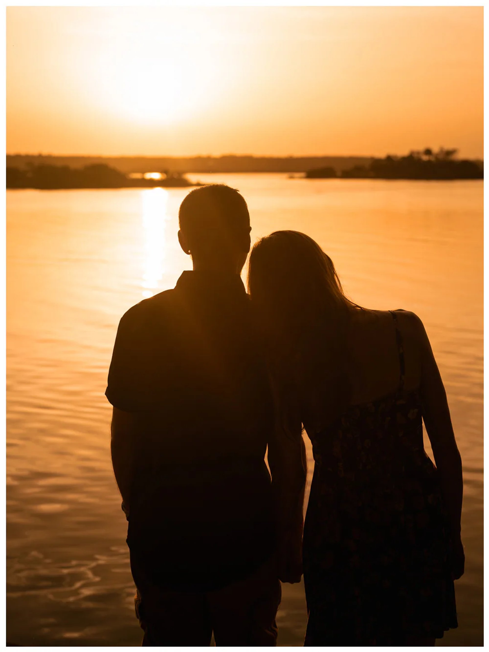 Silhouetted couple standing together beside the river during a Washington Oaks sunset photo session.