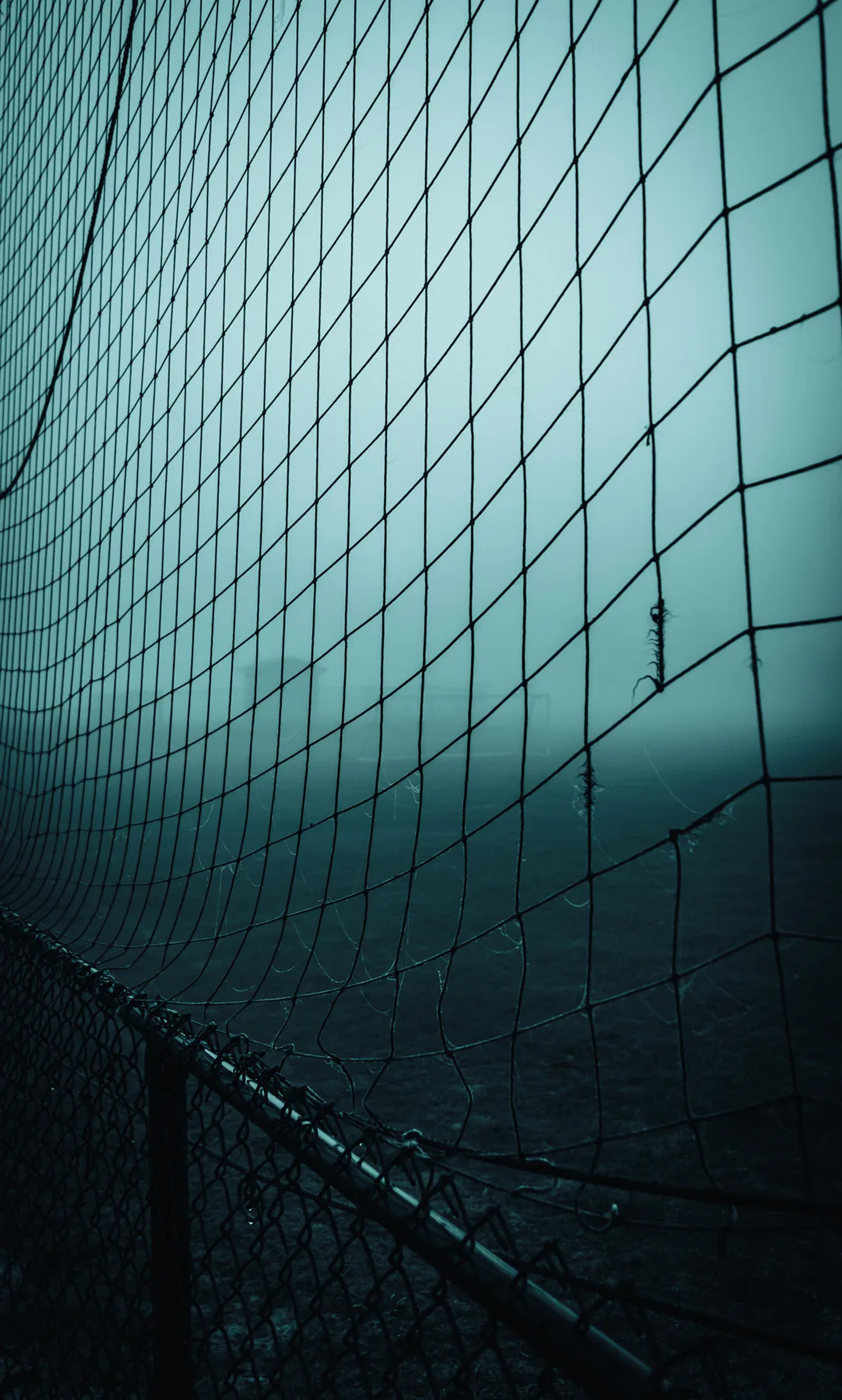 Chain-link fence disappearing into dense blue fog.