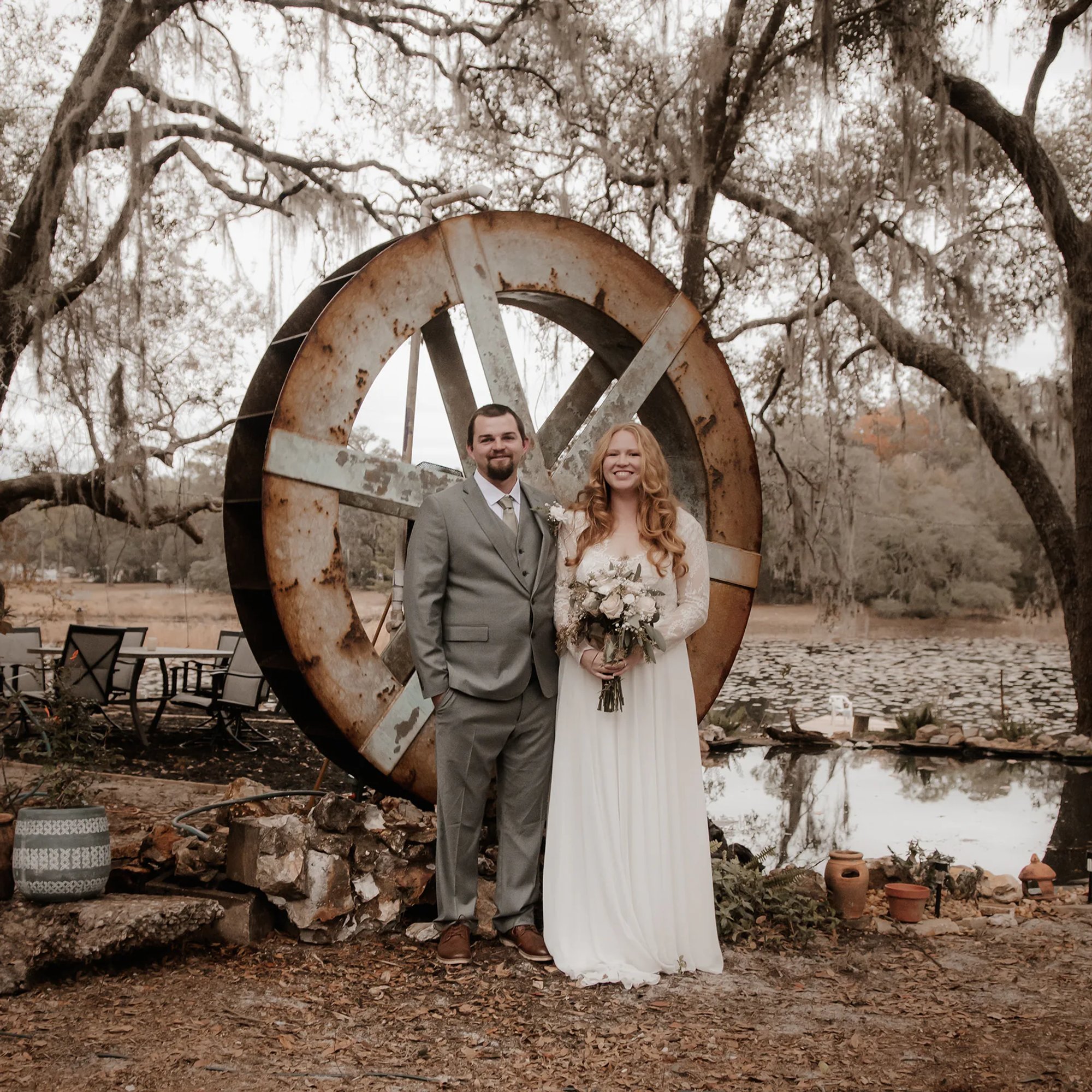 Bride and groom posing in front of a large rustic wooden wheel.