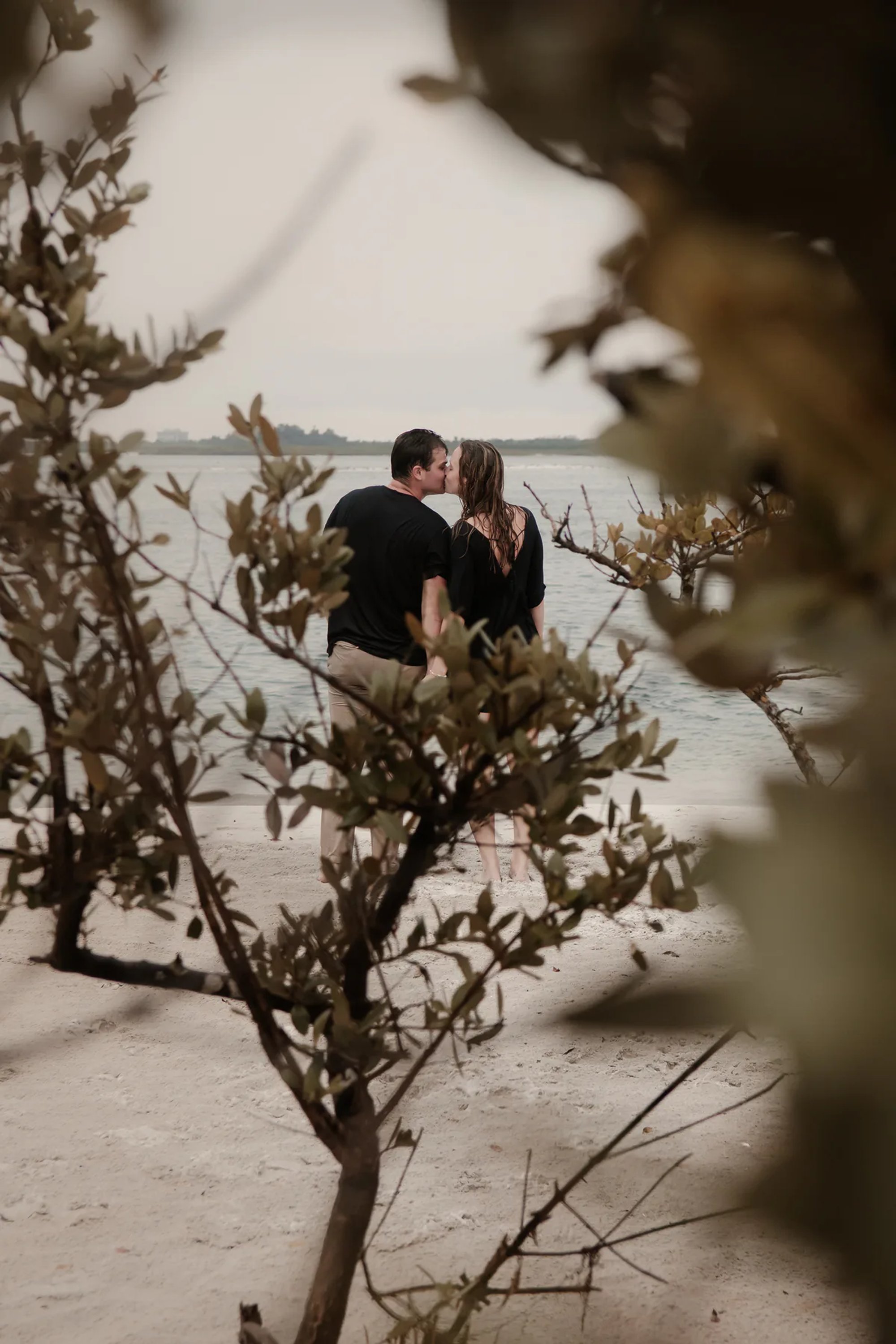 Candid Ponce Inlet engagement photo of couple kissing through beach greenery