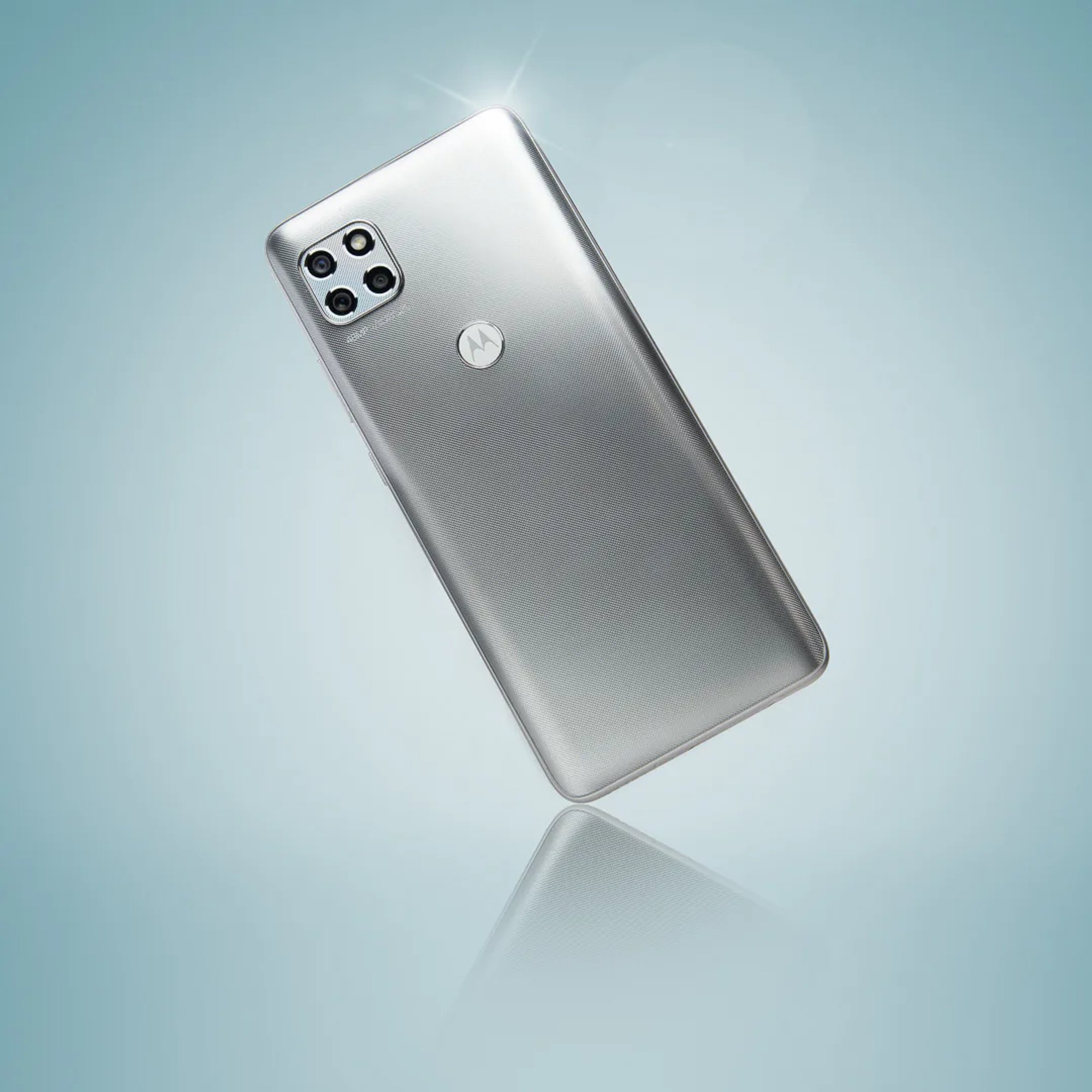 Silver Motorola smartphone reflected on a pale blue surface.