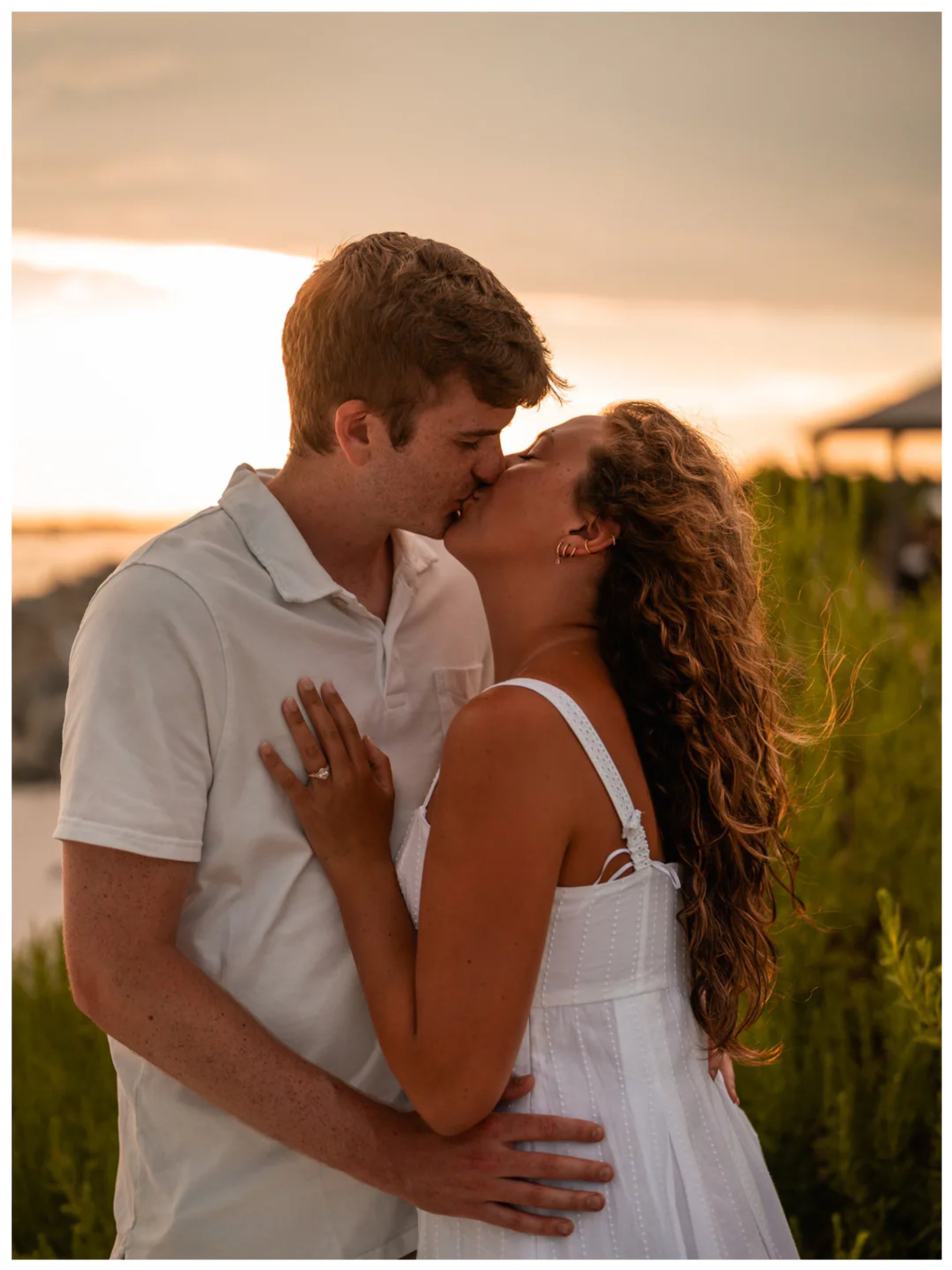 Couple kissing in soft golden light near the beach.