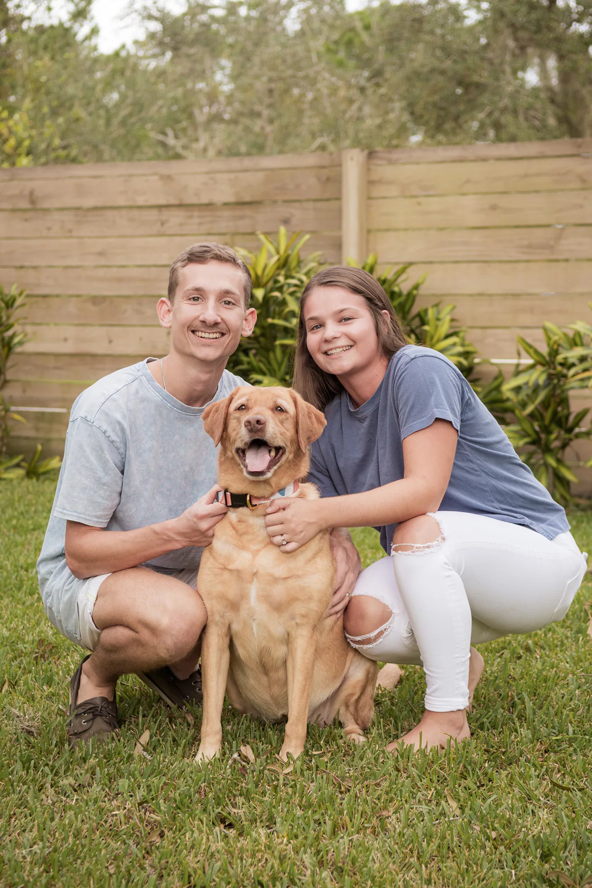 Smiling couple embracing their golden retriever.