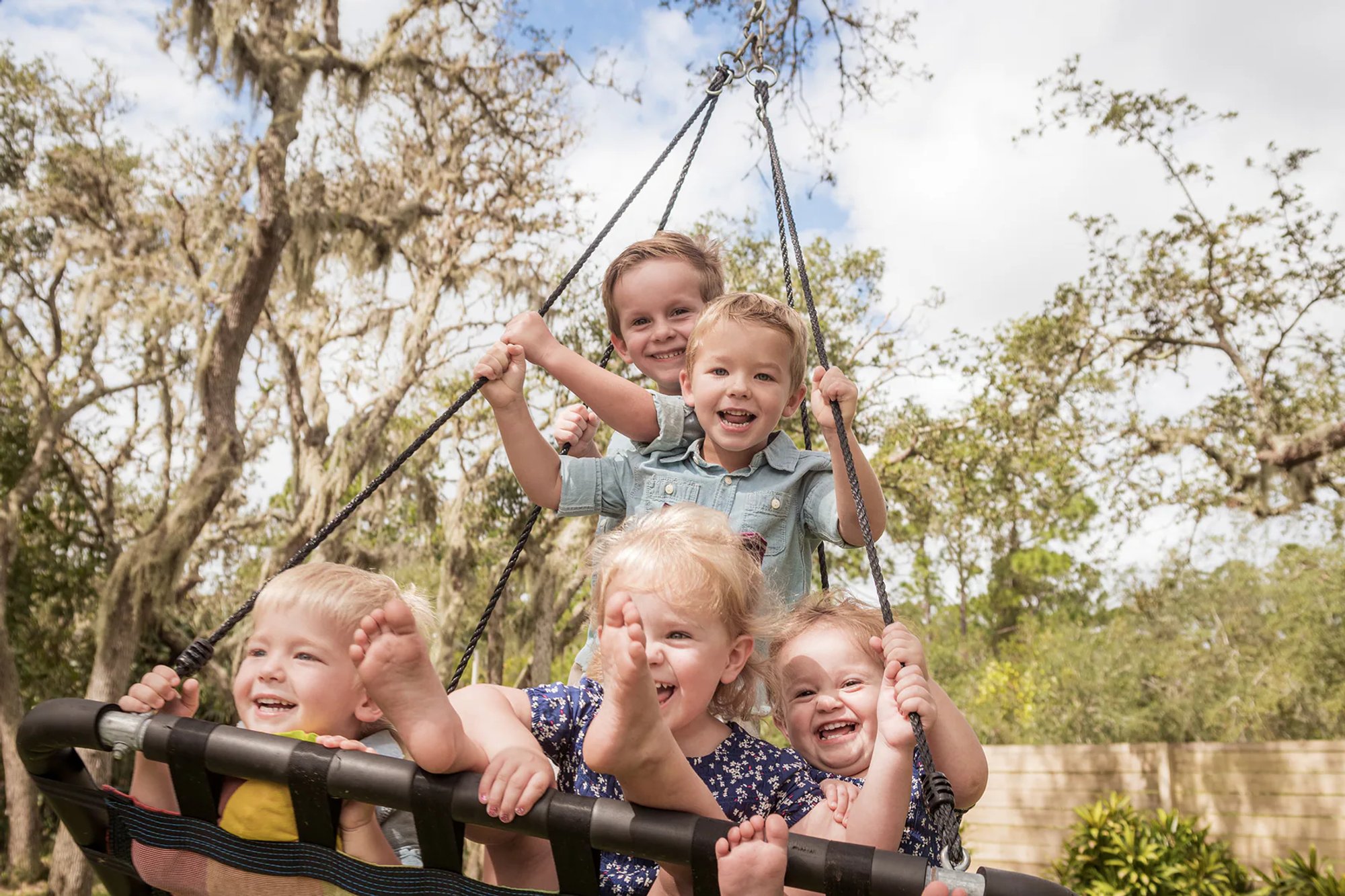 Young children laughing together on a large outdoor swing.