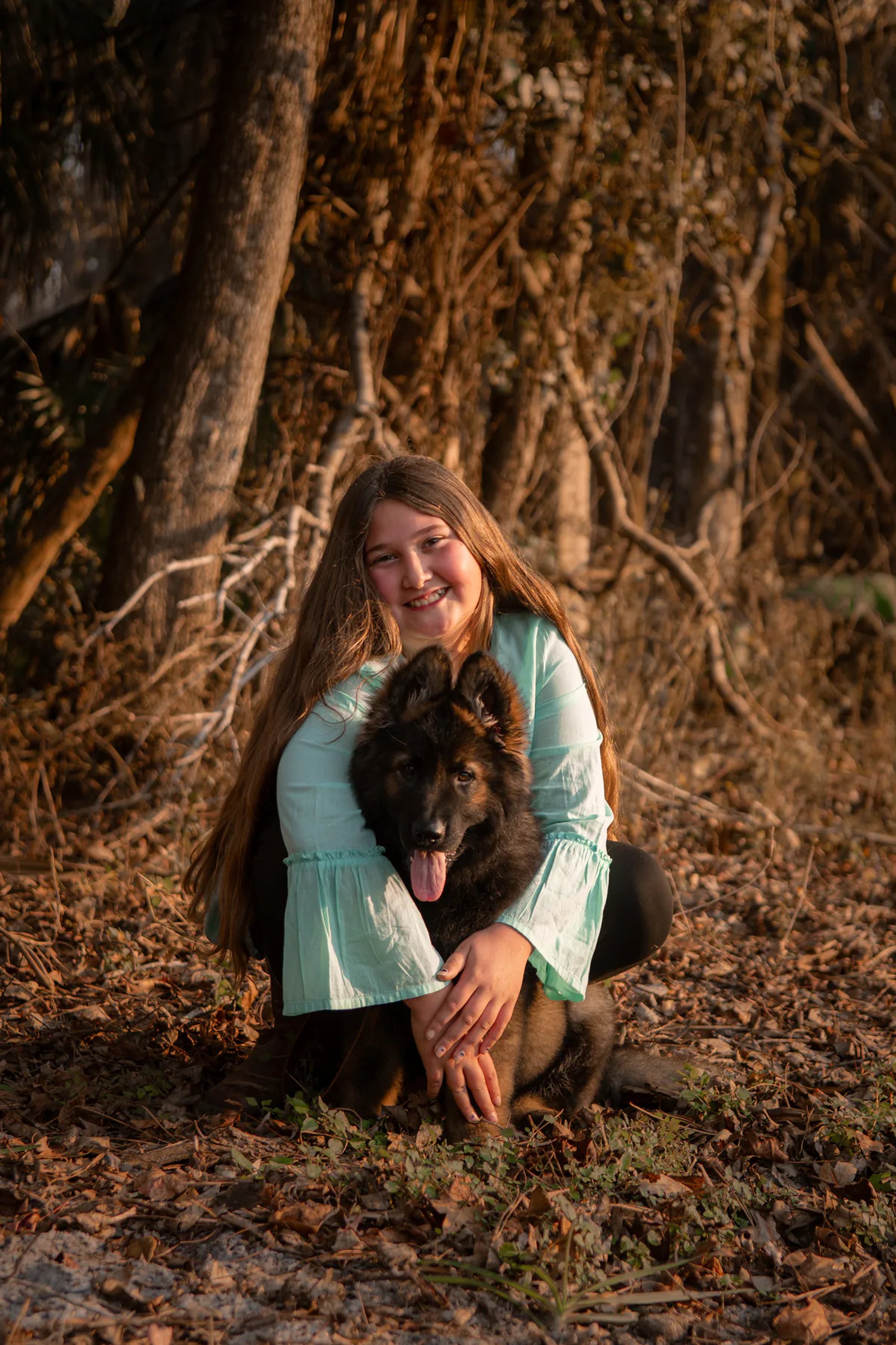 Young woman kneeling with her black dog beneath a large tree.