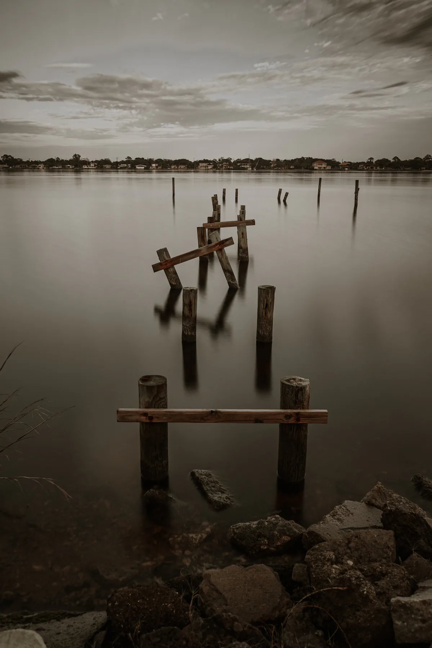 Broken wooden dock posts extending into calm water beneath an overcast sky.